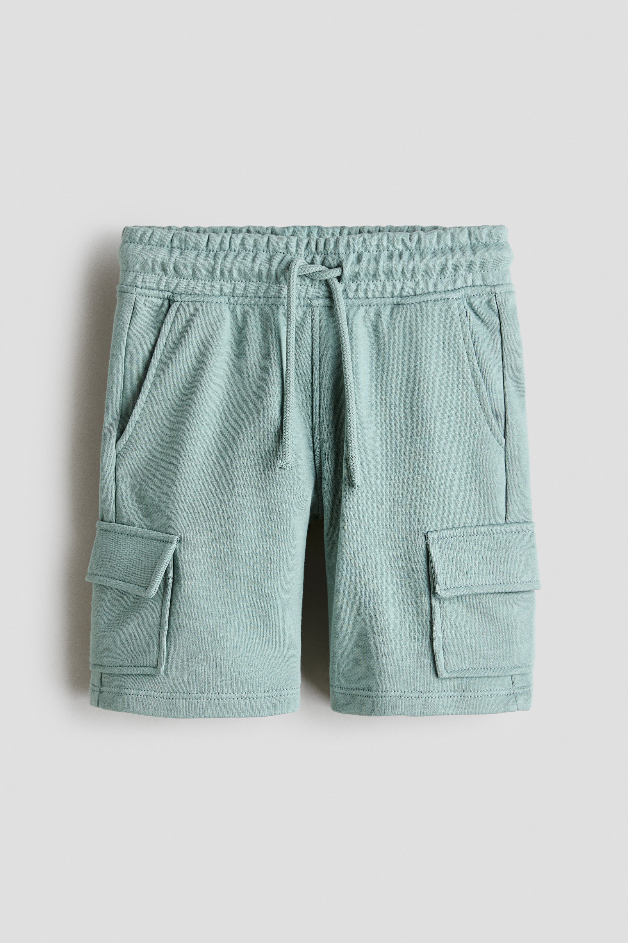Ver imagen más grande: Los pantalones cortos cargo a la altura de la rodilla se presentan desde el frente, confeccionados en un tejido de sudadera ligero de color azul verdoso claro, con una cintura elástica y cordón ajustable, bolsillos laterales diagonales y bolsillos con solapa en cada pierna.