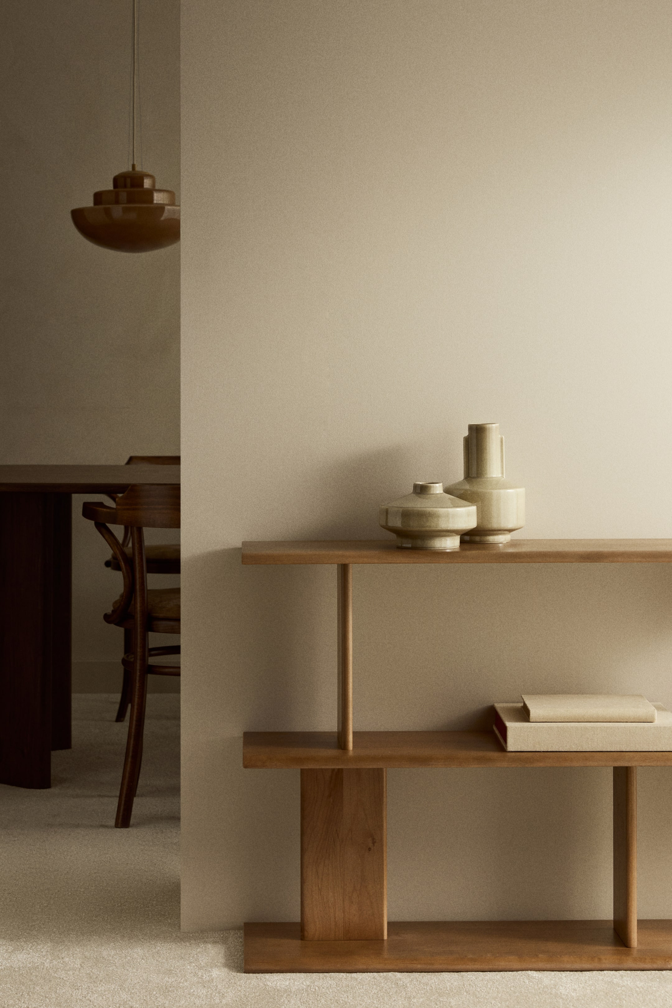 Grotere afbeelding bekijken: Het houten rek staat FRONT gericht, met twee horizontale planken en een asymmetrische indeling van verticale houten steunen. Twee keramische vazen worden op het bovenste oppervlak tentoongesteld en twee boeken op de onderste plank.