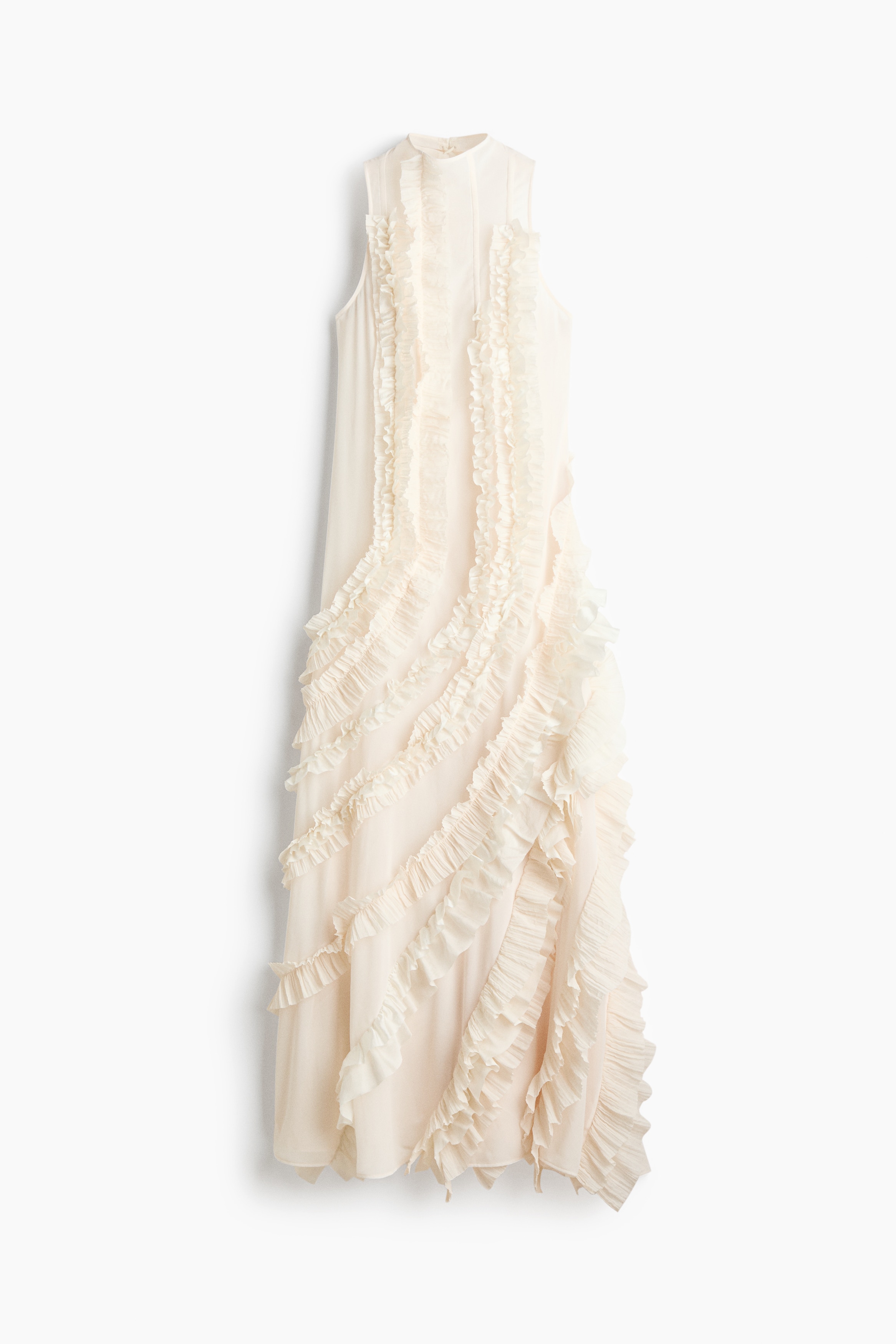 La modelo lleva un vestido maxi sin mangas de color crema, con cuello alto y costuras con volantes en cascada que recorren el cuerpo en curvas para crear una silueta voluminosa y texturizada. El vestido se combina con sandalias de tacÃ³n alto a juego en color crema.