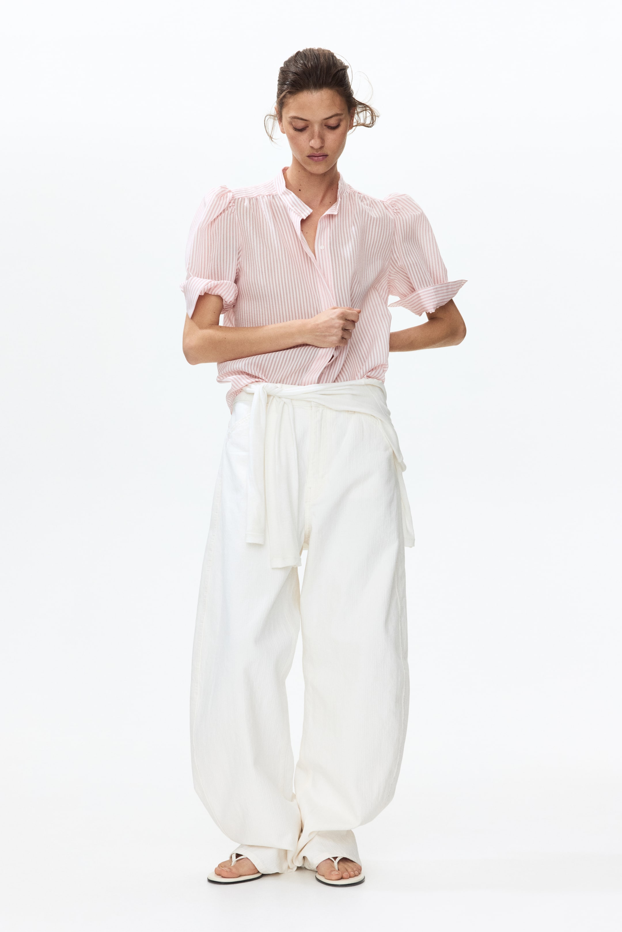 Agrandir l'image: Chemise à rayures roses et blanches avec un col officier, manches courtes bouffantes et poignets retroussés, portée rentrée dans un pantalon blanc à jambes larges. Le pantalon présente une texture verticale subtile et est noué à la taille avec une ceinture en tissu blanc.