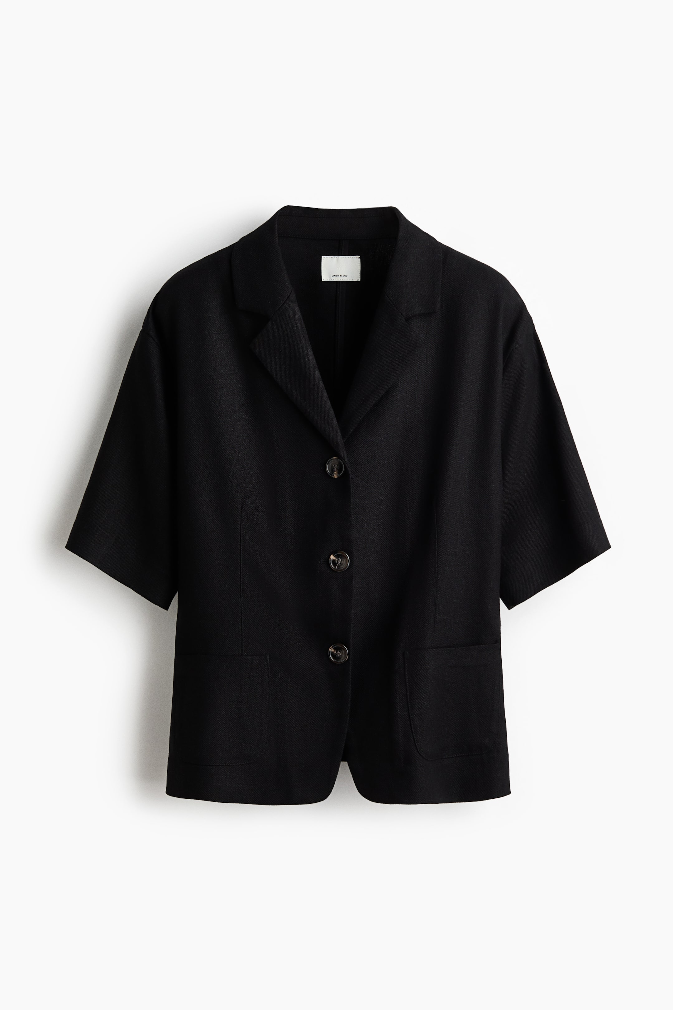 View larger image: A black short-sleeved, single-breasted blazer is showcased from the front, highlighting its airy weave, notch lapels, and three dark brown buttons along the front. Two open patch pockets and shaping darts can be seen at the front.