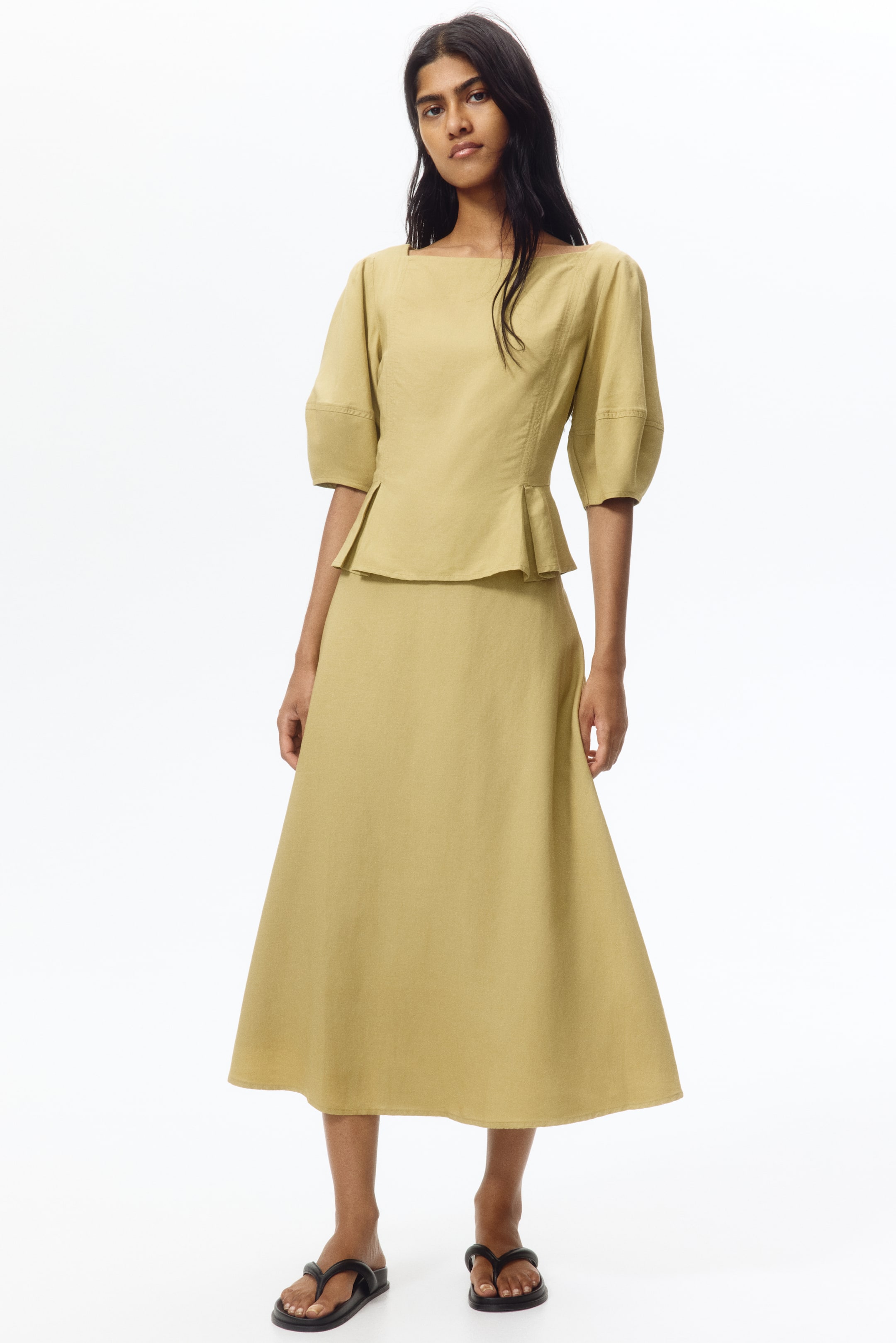 View larger image: A light olive green matching set is being showcased from a front angle, featuring a top with a square neckline, elbow-length puffed sleeves, and a peplum hem, paired with an A-line midi skirt.