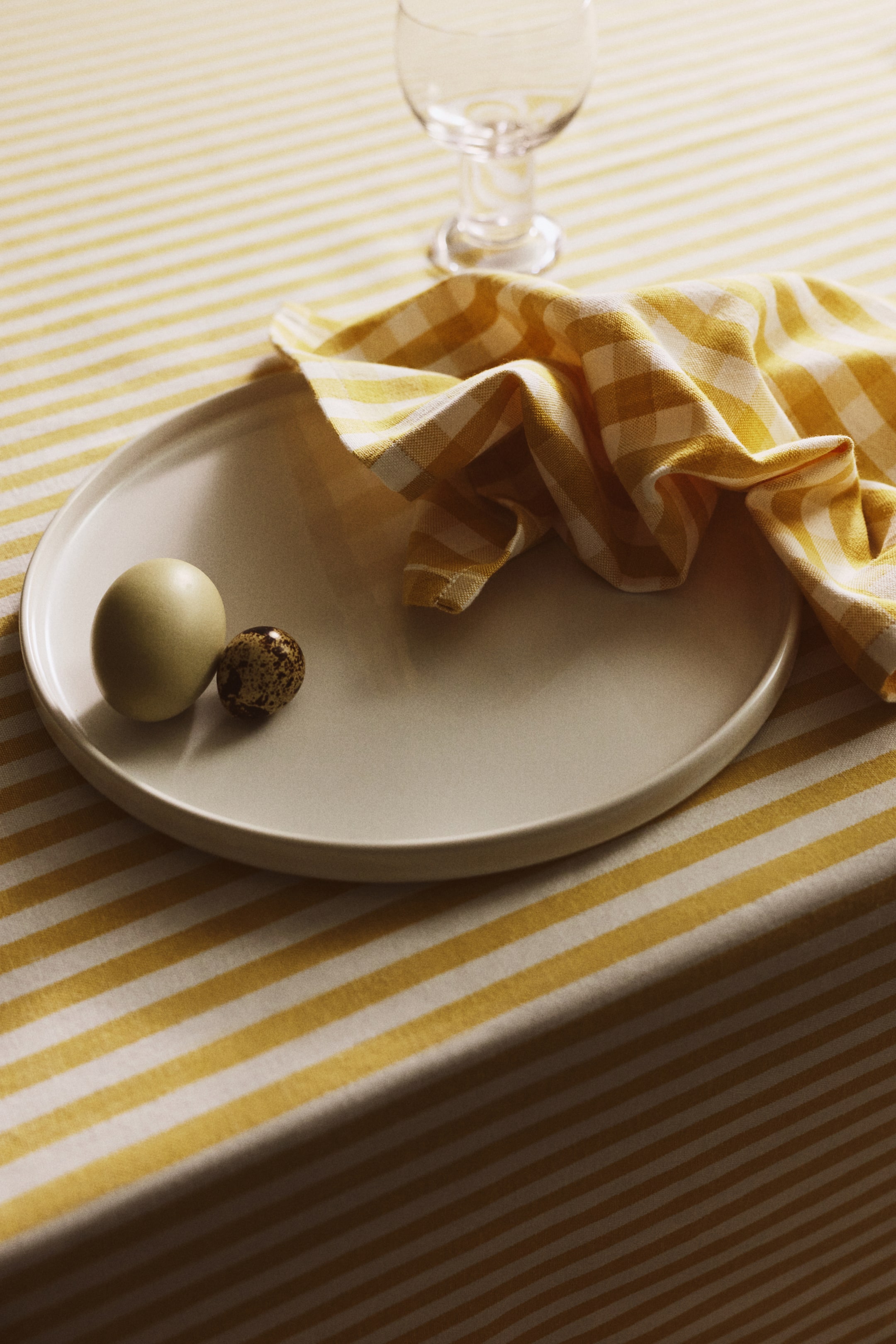 View larger image: A napkin from the pack features a yellow and white gingham pattern on a cotton weave. Its neatly hemmed edges are visible as it's presented folded and draped.