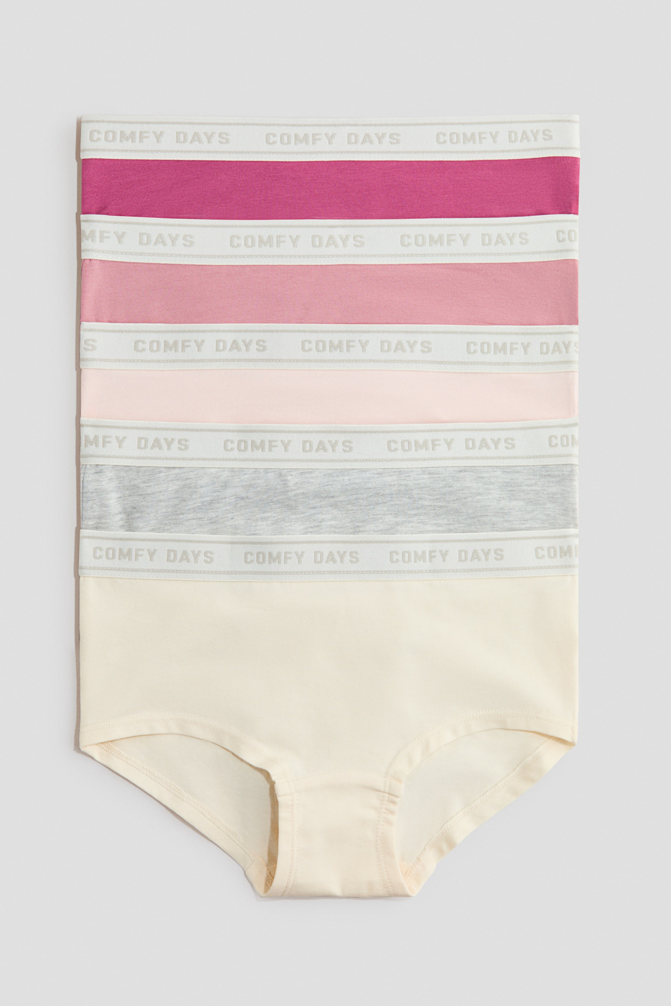 Näytä suurempi kuva: Viisi paria hipster-tyylisiä alushousuja on pinottu etupuoli näkyvissä, jokaisessa on pehmeää puuvillajerseykangasta, näkyvä "COMFY DAYS" -tekstillä varustettu vyötärönauha ja vuorattu haaraosa. Alushousut ovat esillä väreissä fuksia, keskipinkki, vaaleanpunainen, vaaleanharmaa ja kerma.