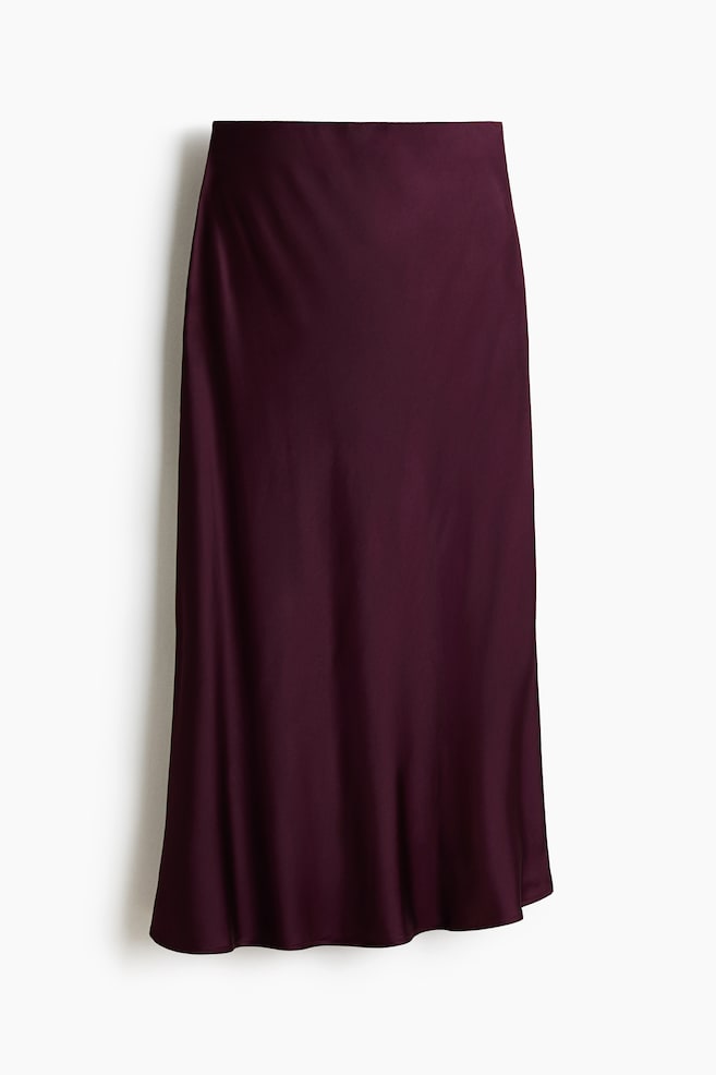 A midi skirt is displaying its front view, featuring a softly draping weave in a deep plum color. It is showing concealed elastication at the waist and a gently flared hem. - 1