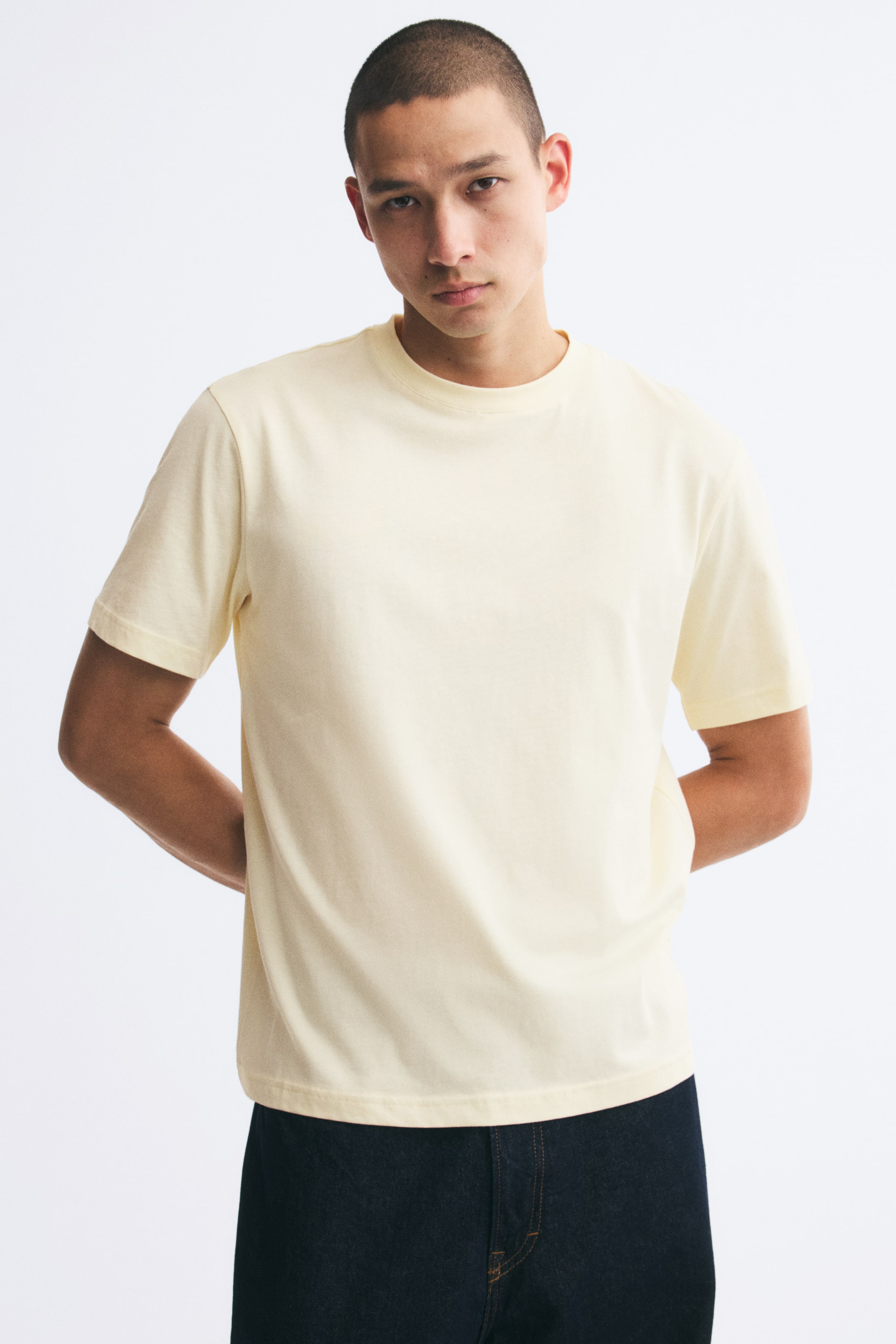 Größeres Bild ansehen: Ein hellgelbes T-Shirt aus leichtem Baumwolljersey wird vom Model getragen und verfügt über einen Rundhalsausschnitt mit Rippbündchen, kurze Ärmel und einen gerade geschnittenen Saum. Das T-Shirt in Regular Fit ist mit dunkelblauer Denim-Hose kombiniert.