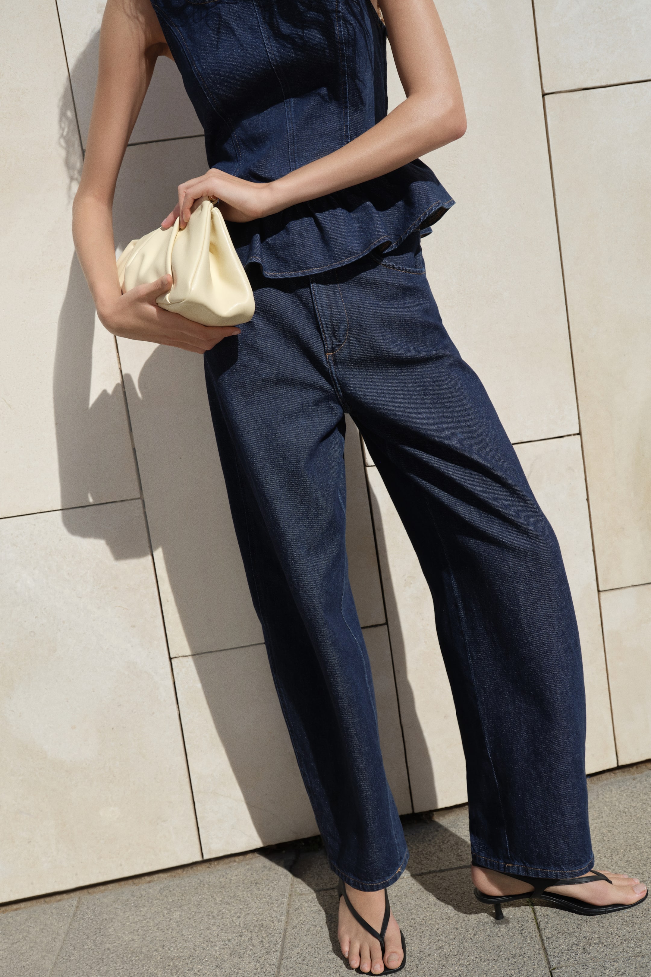 View larger image: Dark wash wide-leg denim pants featuring a high-rise waist, front pockets, and contrast stitching, presented from a slight angle to highlight their relaxed fit.
