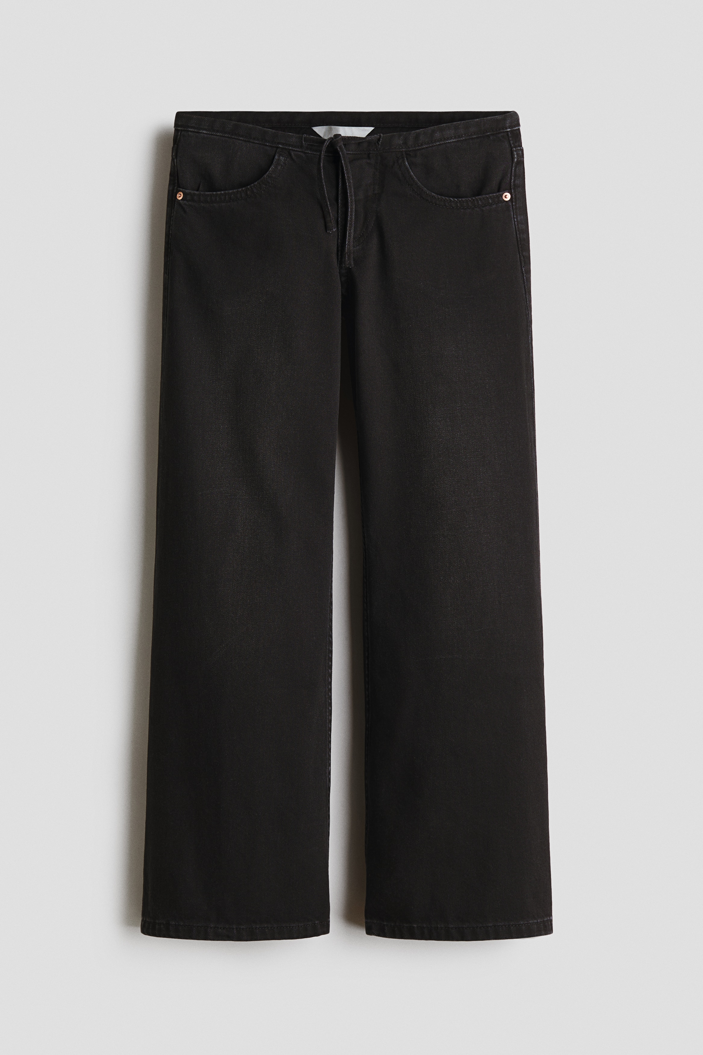 Jeans i mÃ¸rkvasket bomuldsdenim vises forfra med en lÃ¸s pasform over hofterne og ekstra vide ben, der falder ned over skoene. Det lavtaljede design sidder afslappet under en bordeaux sweater og fremhÃ¦ver deres slouchy silhuet.
