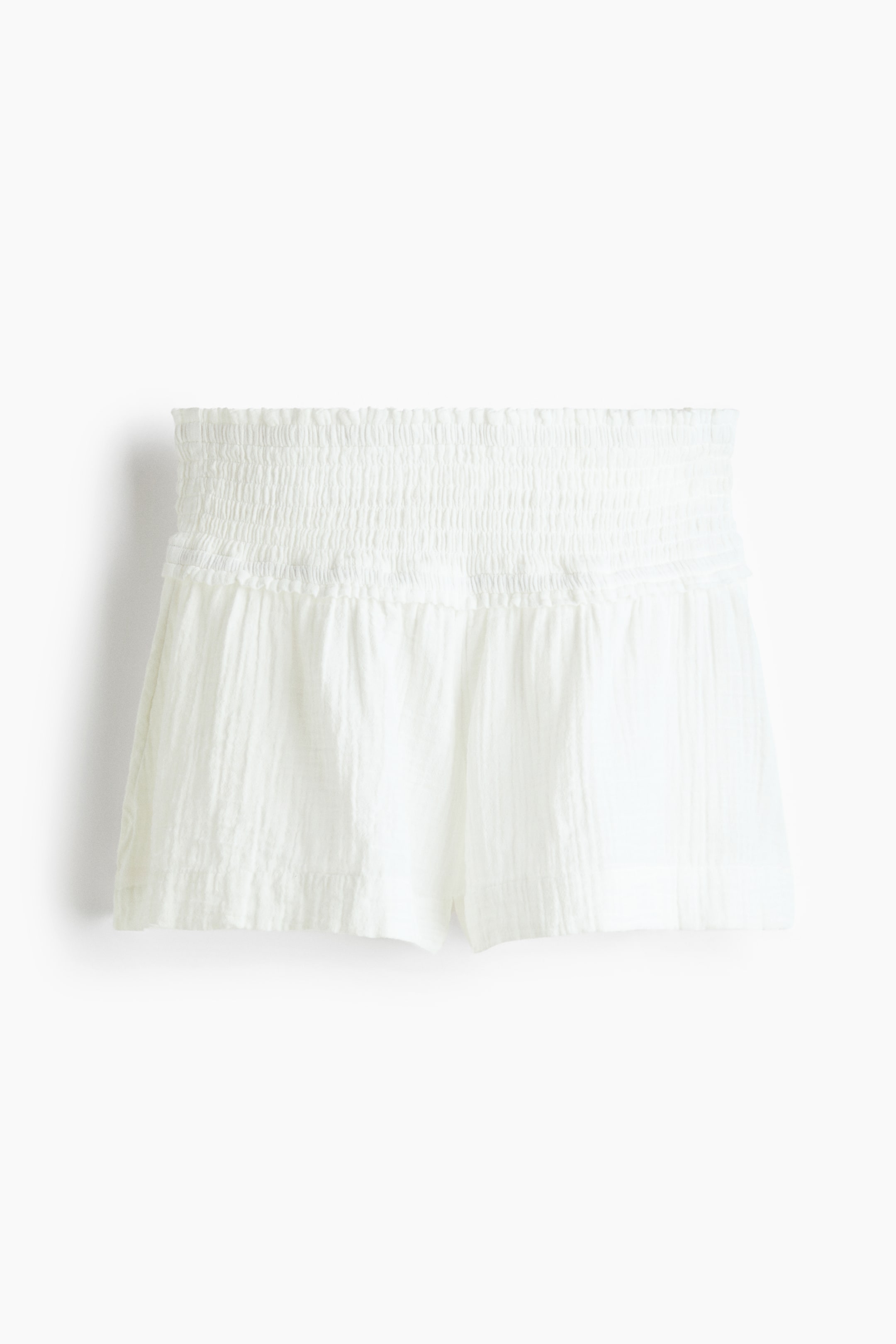 Ver imagen más grande: Los pantalones cortos blancos presentan una cintura ancha y fruncida, con una textura arrugada en toda la tela. Los pantalones cortos muestran un ajuste suelto y corto cuando se ven desde el frente.