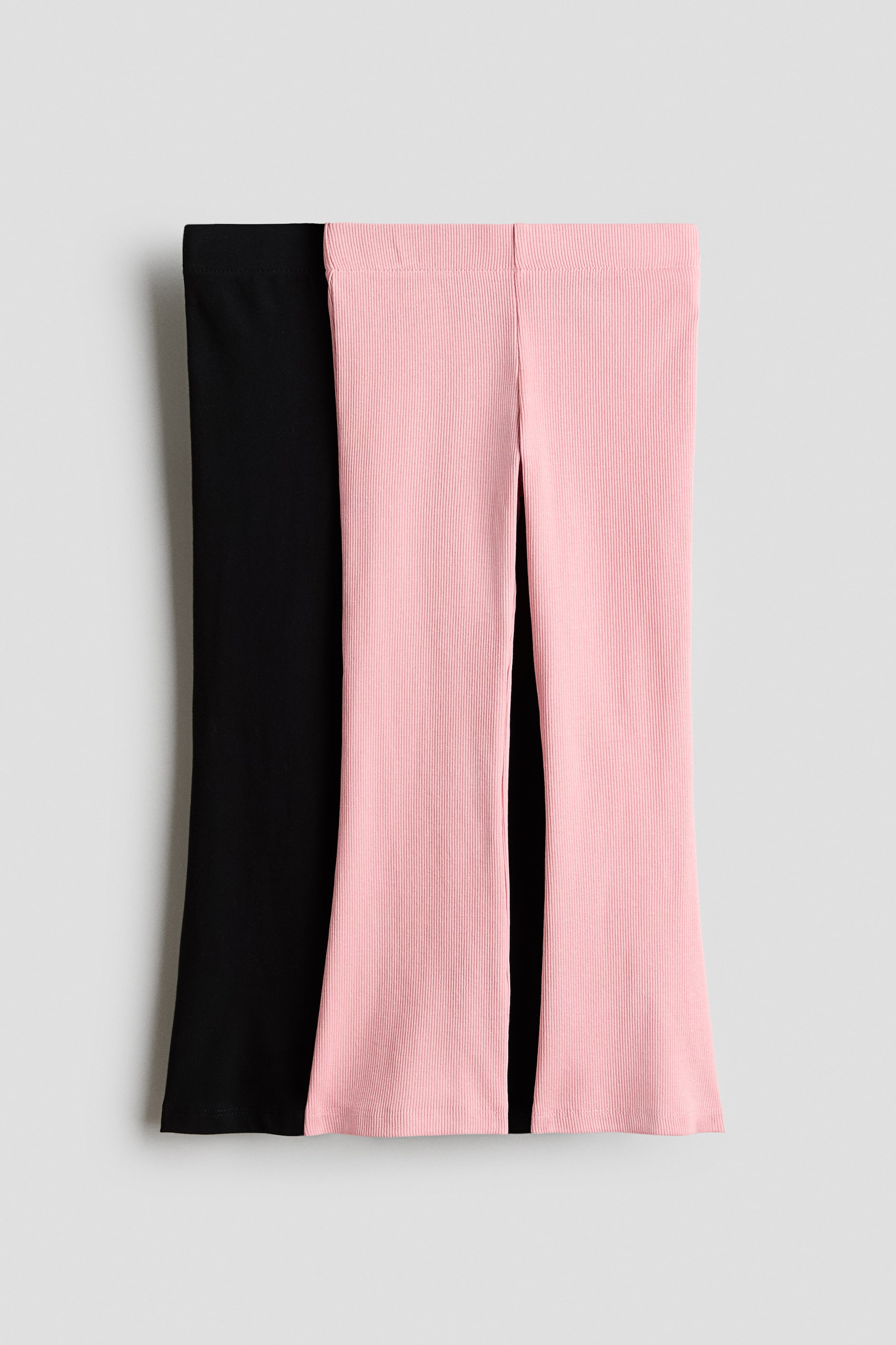 View larger image: Two pairs of front-facing trousers are displayed, with a black pair layered beneath a pink ribbed pair. The black trousers boast a smooth texture, while the pink ones feature a ribbed knit. Both showcase a wide-leg cut complemented by a simple waistband.