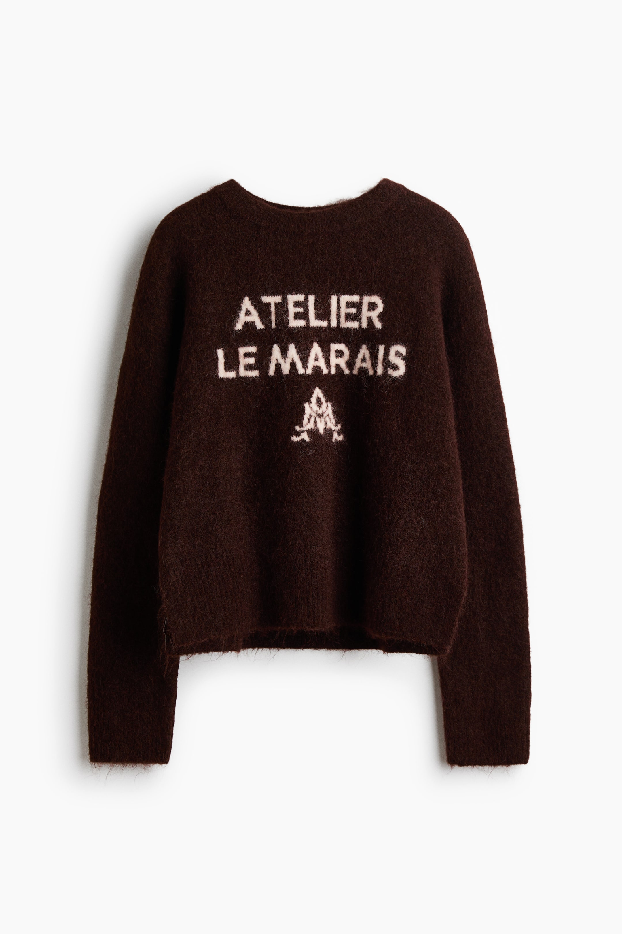 Ver imagen más grande: Un jersey marrón oscuro está extendido, mostrando una textura de punto peludo y un cuello redondo. En su parte frontal aparece el texto blanco "ATELIER LE MARAIS" junto a un gráfico estilizado en blanco.