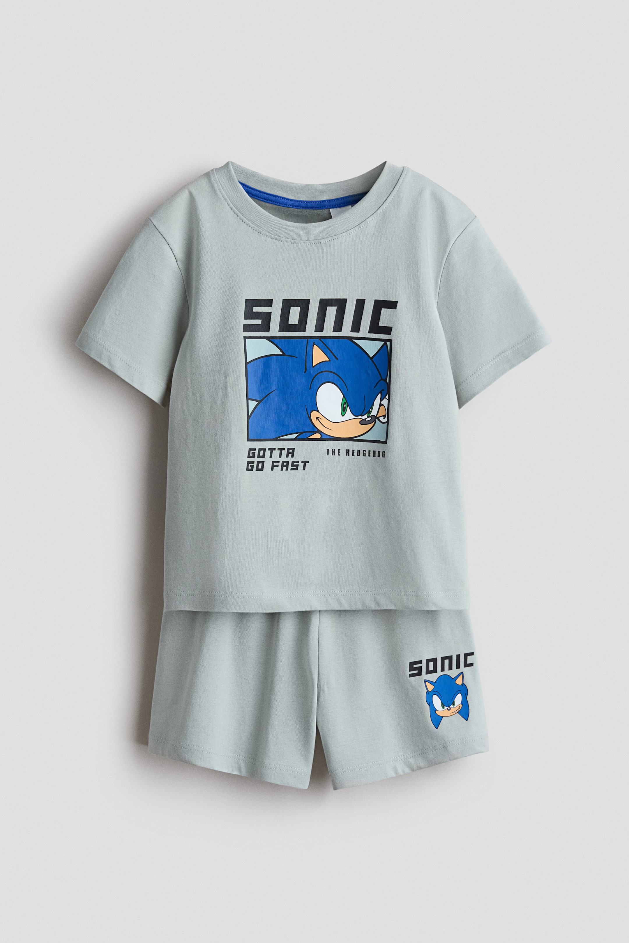 Agrandir l'image: Un ensemble de pyjama vert clair est présenté de face, comprenant un t-shirt et un short assorti en jersey de coton imprimé doux. Le t-shirt arbore un grand imprimé graphique de Sonic the Hedgehog et une bordure côtelée autour de l'encolure, tandis que le short est conçu avec une taille élastiquée et affiche un plus petit graphique assorti de Sonic.