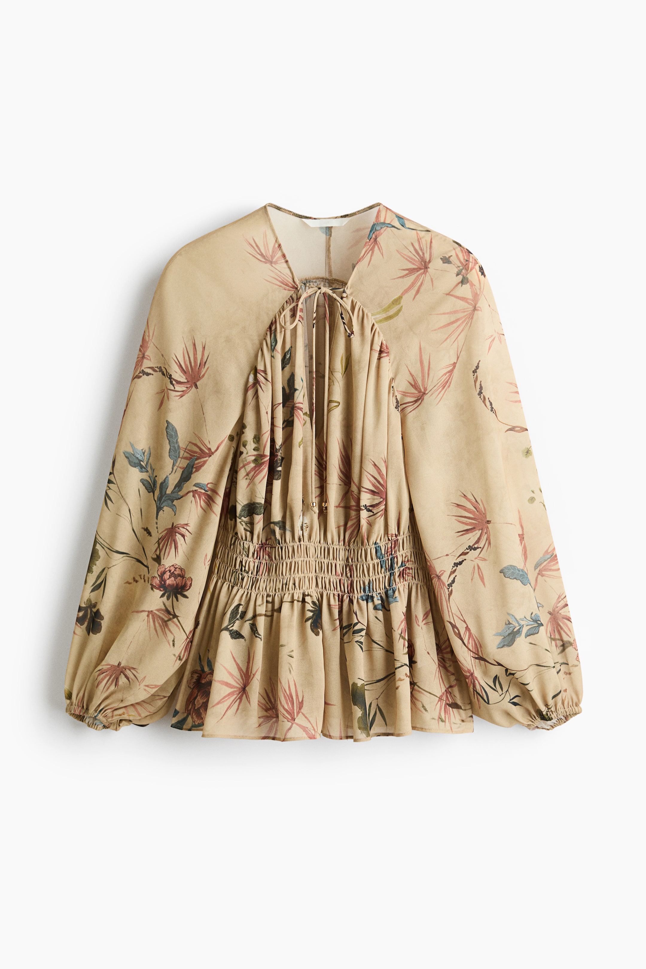 Ampliar la imagen: Una blusa beige de frente con un sutil estampado floral presenta un escote en V profundo con lazos delgados, fruncido en los hombros y mangas largas tipo globo con puños elásticos. La blusa muestra una cintura fruncida que se abre en un dobladillo con volantes.