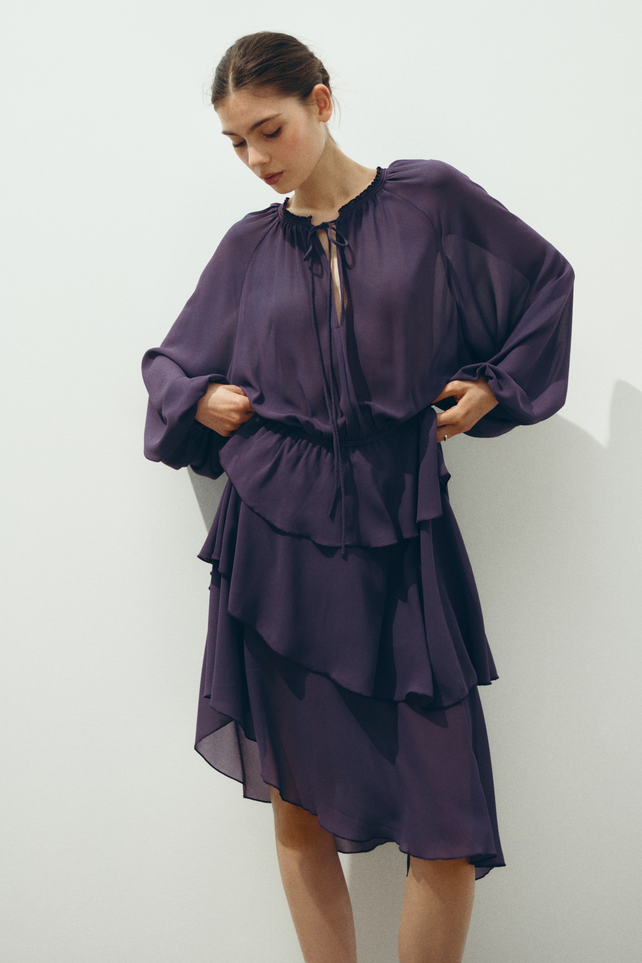 Ver imagen más grande: Vestido púrpura translúcido con un escote fruncido de cordón y apertura en V, mangas largas voluminosas, cuerpo blusón y una falda midi con volantes en capas y un dobladillo asimétrico.