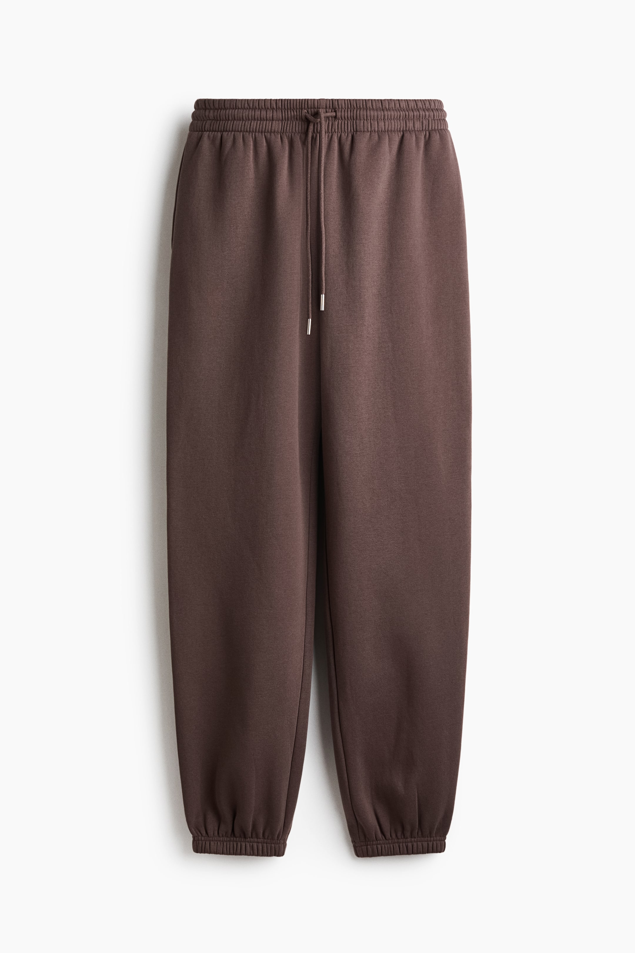 View larger image: A pair of dark brown track pants is shown from the front, featuring a high, elastic waistband with a matching drawstring. The pants have a relaxed fit, tapering down to gathered elastic cuffs at the hems.
