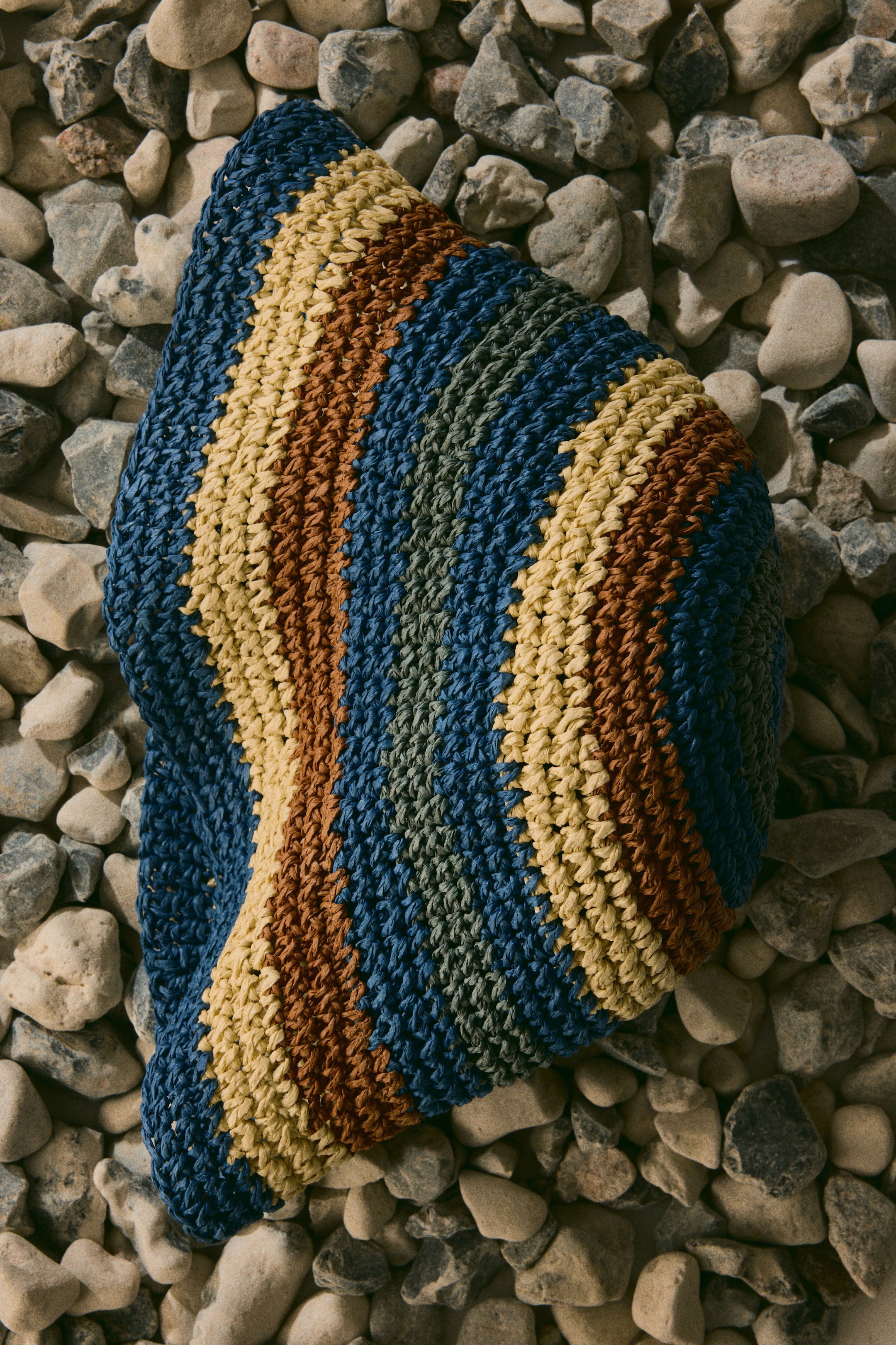 View larger image: The product, a textured woven item, showcases diagonal stripes in shades of blue, light yellow, rust brown, and muted green, viewed from an overhead angle.