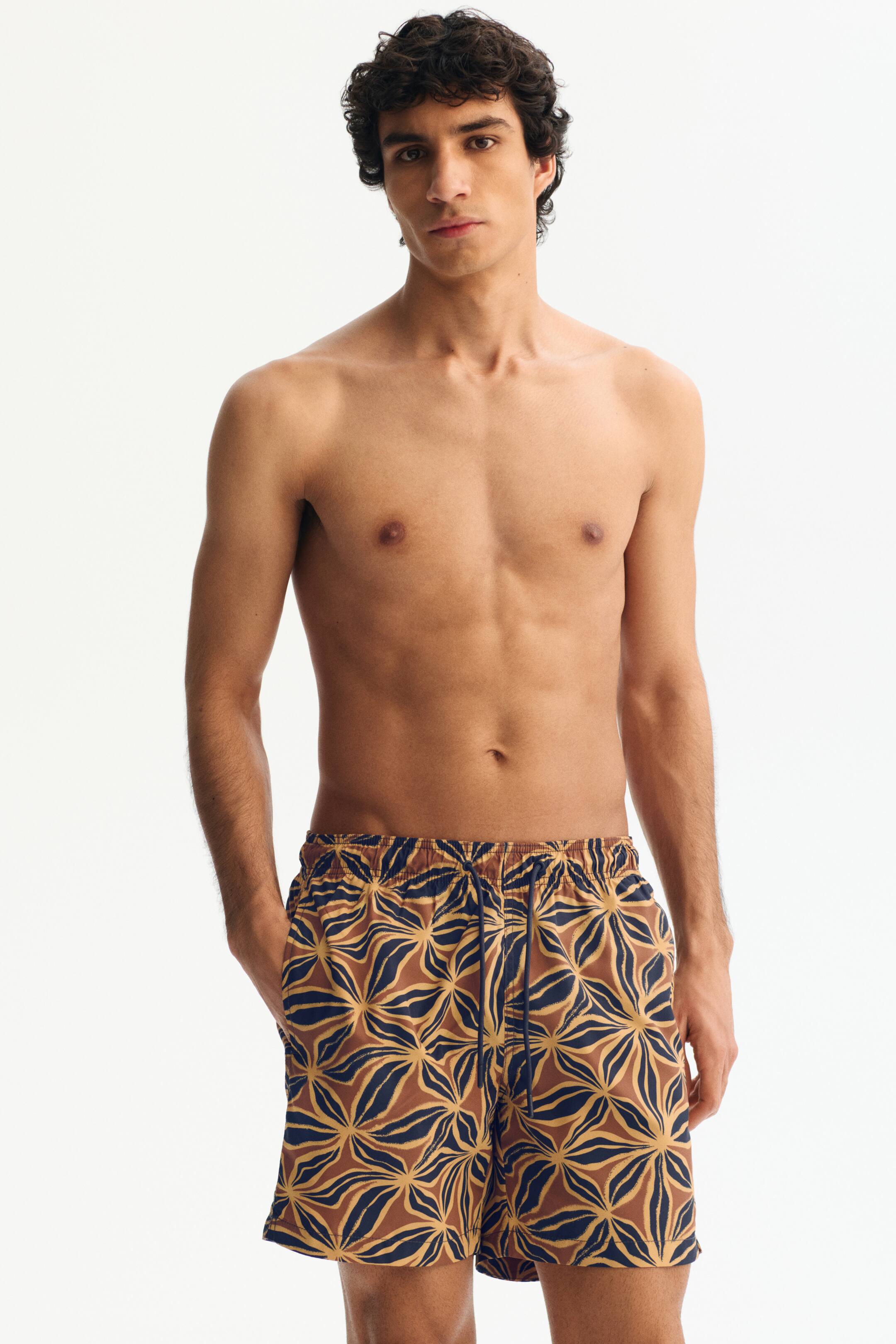 View larger image: Men's swim shorts showcase a striking abstract floral pattern in brown, gold, and dark blue hues. Crafted with an elasticated waistband, a visible drawstring, and side pockets, they offer a relaxed fit that sits comfortably at mid-thigh.