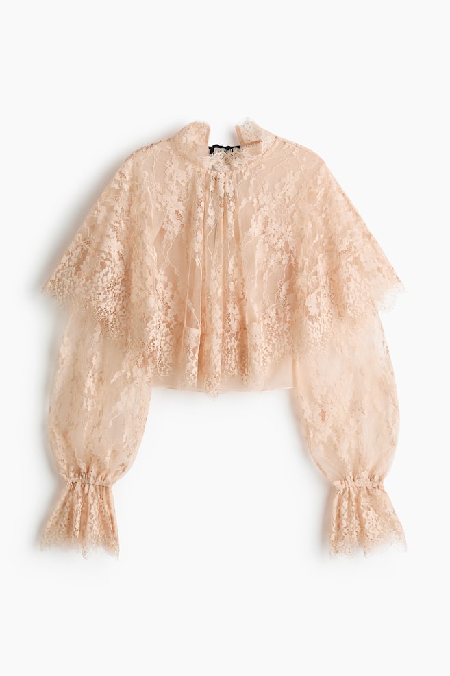 A peach-toned lace blouse is showcasing its front view, featuring a high ruffled collar and a gathered neckline. It is crafted with voluminous balloon sleeves ending in shirred lace cuffs and a cropped, ruffled hem. - 1