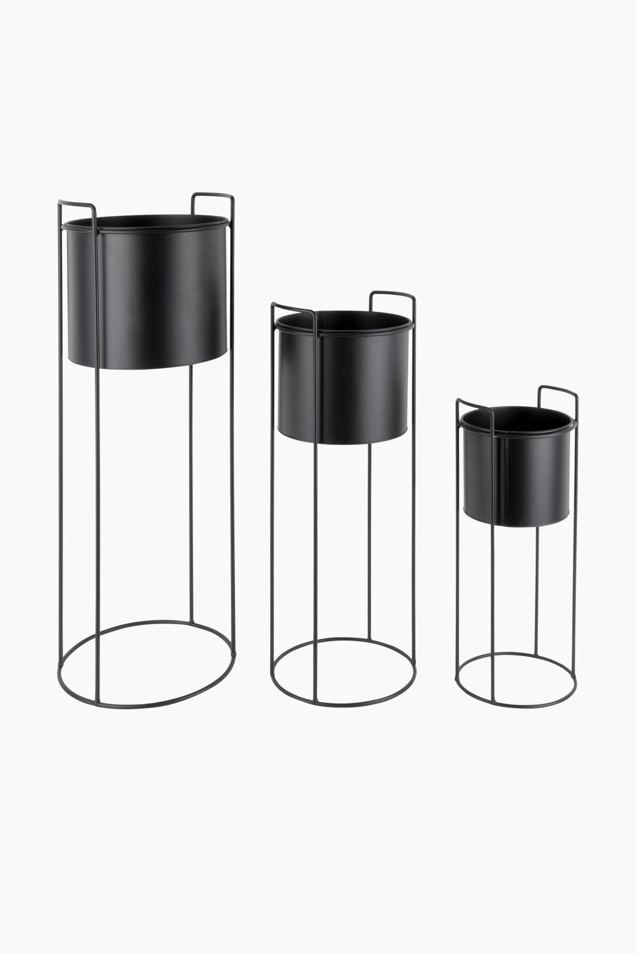 Zobacz większy obraz: Trzy czarne metalowe stojaki na rośliny prezentują się w różnych wysokościach i rozmiarach. Każdy stojak wyposażony jest w cylindryczną doniczkę, która mieści się w smukłej ramie z drutu, tworzącej okrągłą podstawę i zapewniającej wsparcie wokół górnej krawędzi doniczki dzięki dwóm ku górze zakrzywionym przedłużeniom ramy.