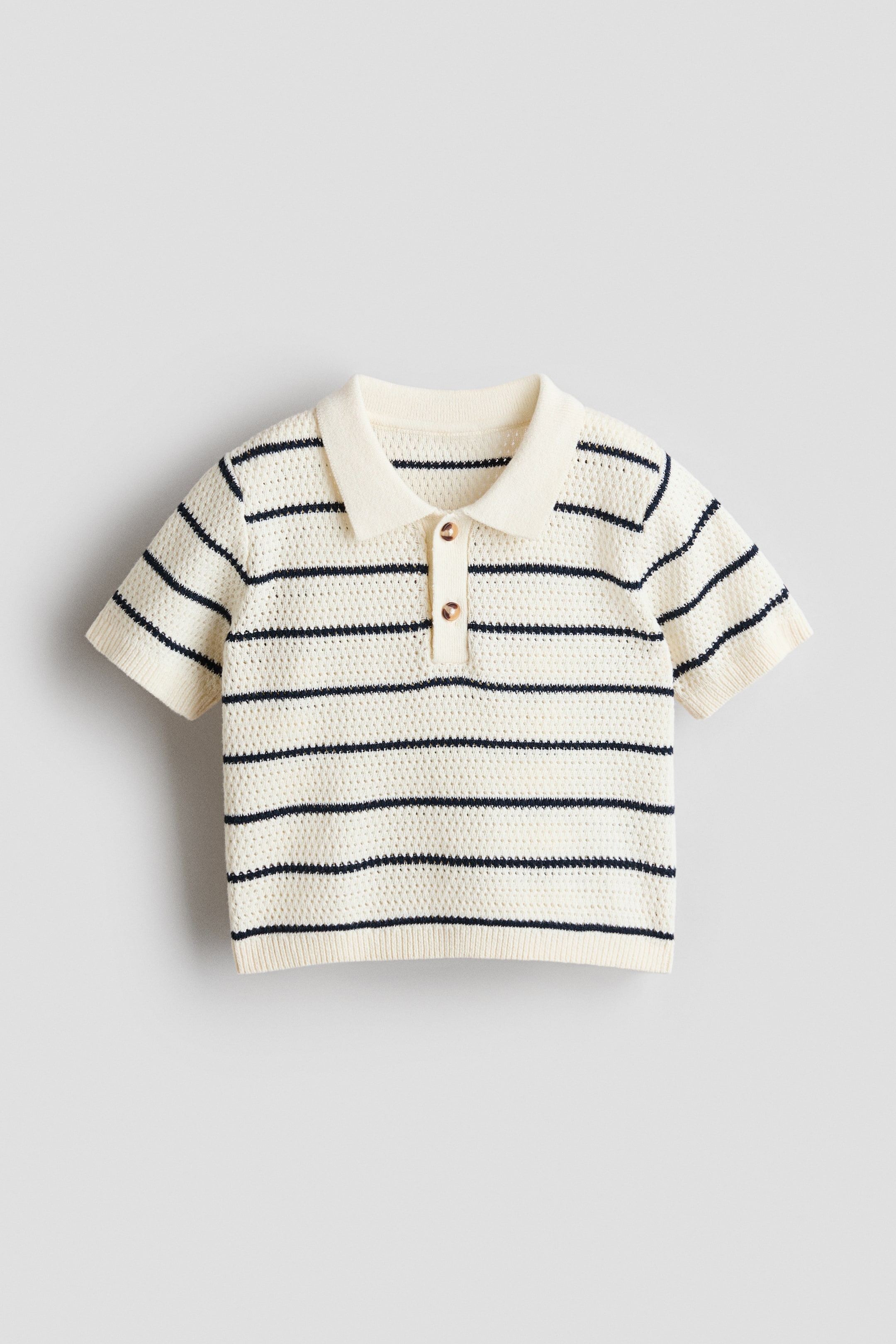Ampliar la imagen: Un polo de manga corta color crema presenta su FRONT, con franjas horizontales azul marino y una textura de punto abierto. Está diseñado con cuello tipo polo, una tapeta de dos botones con botones de color café y puños y dobladillo acanalados.