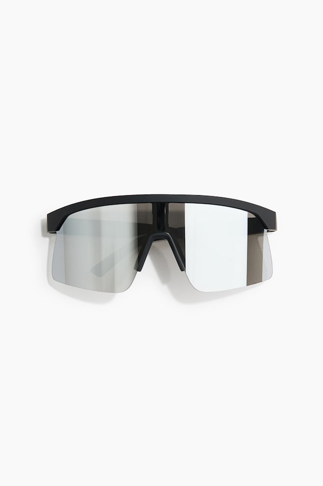 Activewear sunglasses are facing front, featuring a matte black brow bar frame with a single-shield design. The large, reflective silver-mirrored lenses are showing a semi-rimless structure with an integrated black nose bridge. - 1