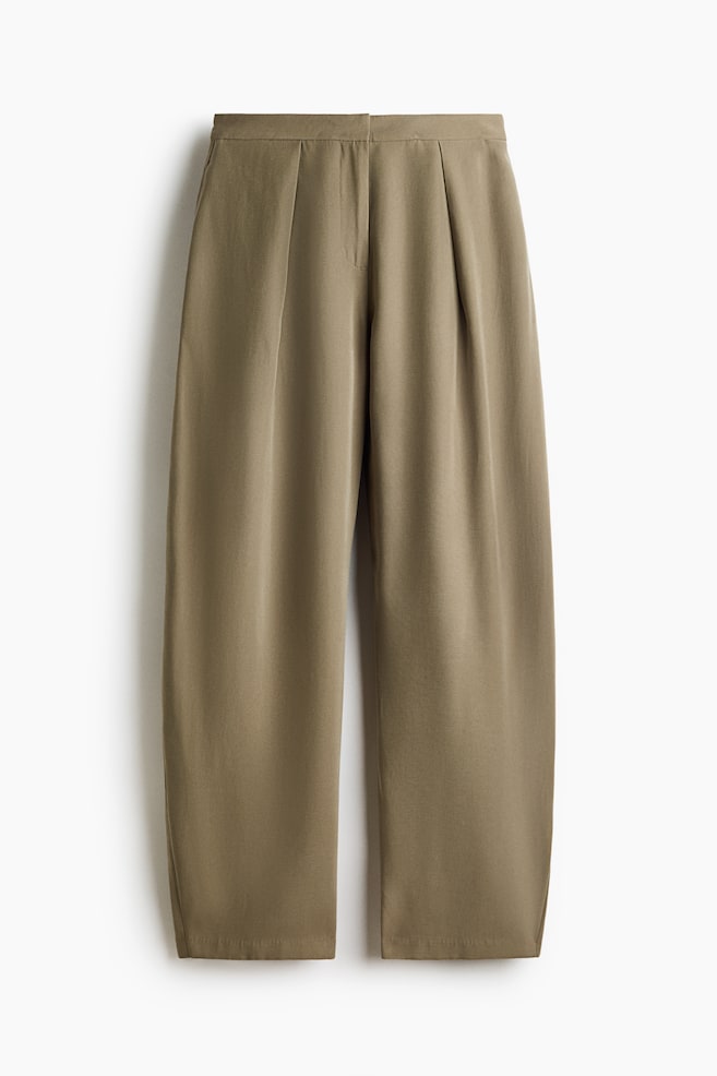 Les pantalons vert olive présentent une ceinture plate avec une fermeture frontale dissimulée, ornés de deux plis avant marquants sur chaque jambe, s'évasant en une silhouette large et raccourcie. - 1