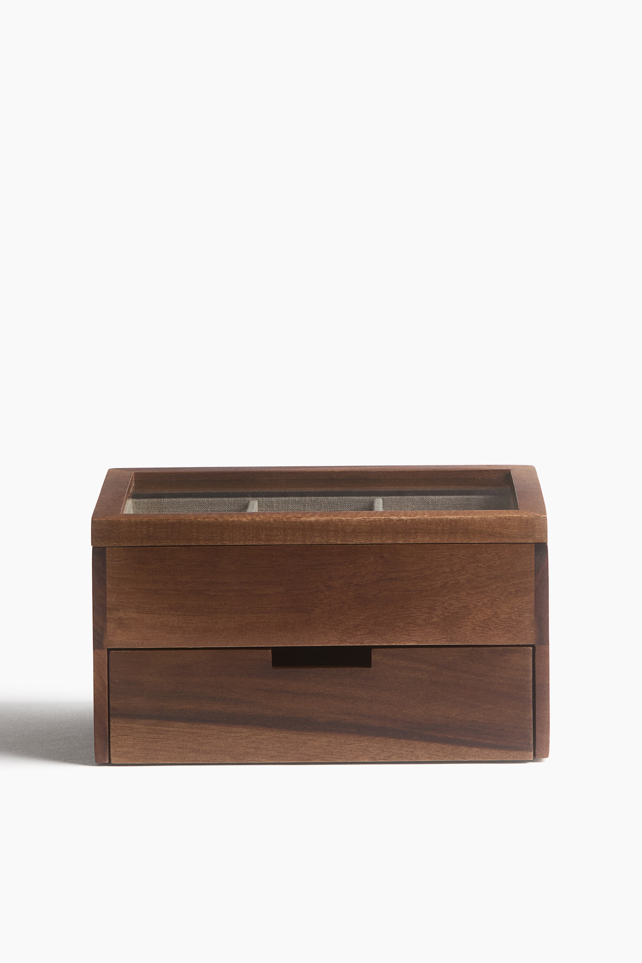 View larger image: A wooden storage box is shown from the front, featuring a top compartment with a rectangular glass window in the lid that reveals grey fabric dividers inside. A single pull-out drawer with a recessed handle is positioned below the main compartment, showcasing the warm brown wood grain of the structure.