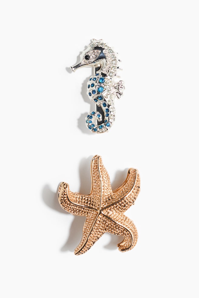 The product is featuring two brooches: a silver-toned seahorse sparkling with clear and blue rhinestones, its head facing left, and a gold-toned starfish displaying a textured, pebbled surface. - 1