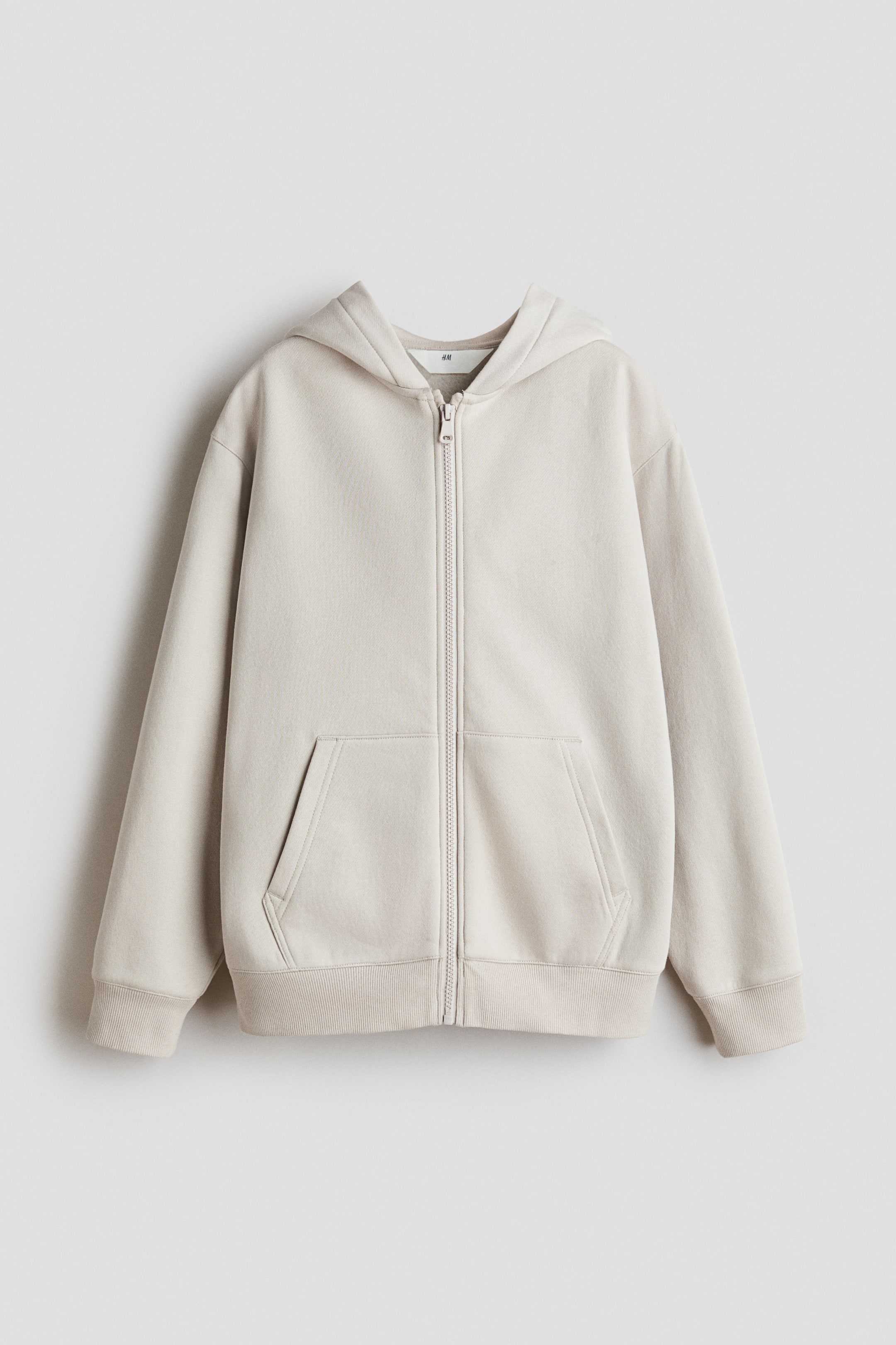 Größeres Bild ansehen: Eine hellfarbene Kapuzenjacke aus Sweatshirtstoff mit Reißverschluss vorne, ausgestattet mit einer gefütterten Kapuze, einem zentralen Reißverschluss, überschnittenen Schultern und zwei aufgesetzten Vordertaschen. Abgerundet wird das Design durch gerippte Bündchen und einen gerippten Saum.