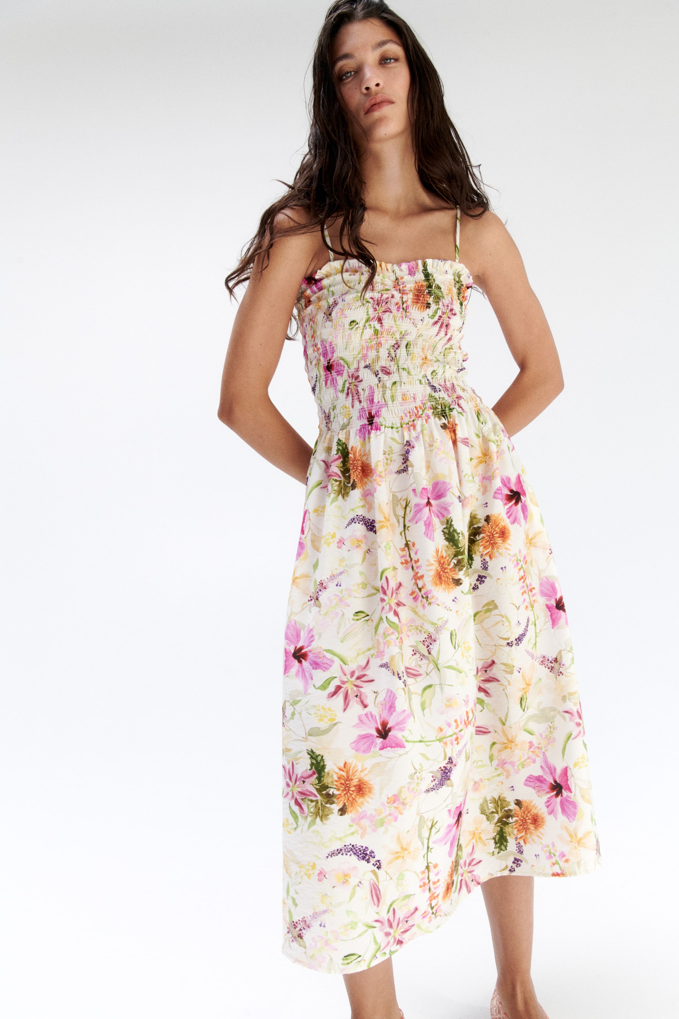 View larger image: An off-white midi dress featuring a shirred bodice and delicate spaghetti straps showcases a vibrant floral pattern in shades of pink, orange, and purple, with a flowing skirt.