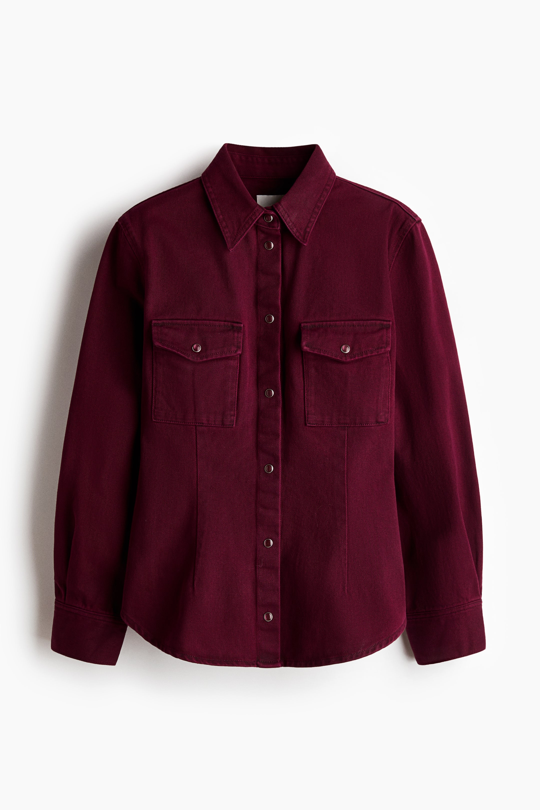 Visualizza immagine più grande: Una camicia in denim bordeaux è mostrata frontalmente, con colletto a punta, chiusura frontale con bottoni a pressione su tutta la lunghezza e due tasche sul petto con patta e chiusura a pressione. Sono inoltre visibili cuciture verticali sotto le tasche sul petto, maniche lunghe con polsini con bottoni a pressione e orlo arrotondato.