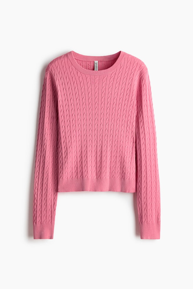 A pink jumper is presented facing FRONT, showcasing a cable-knit pattern across its body and long sleeves. It is featuring a round, ribbed neckline, ribbed cuffs, and a ribbed hem. - 1