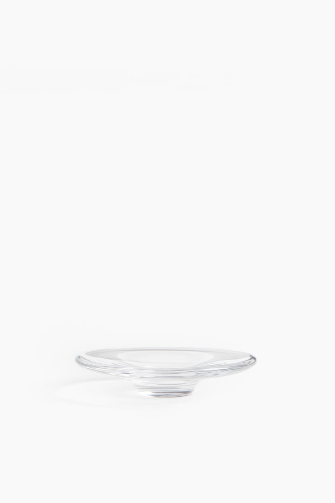 A small bowl, crafted from thick, high-shine clear glass, features a wide, shallow design and rests on a distinct, slightly raised base, visible from the front. - 1