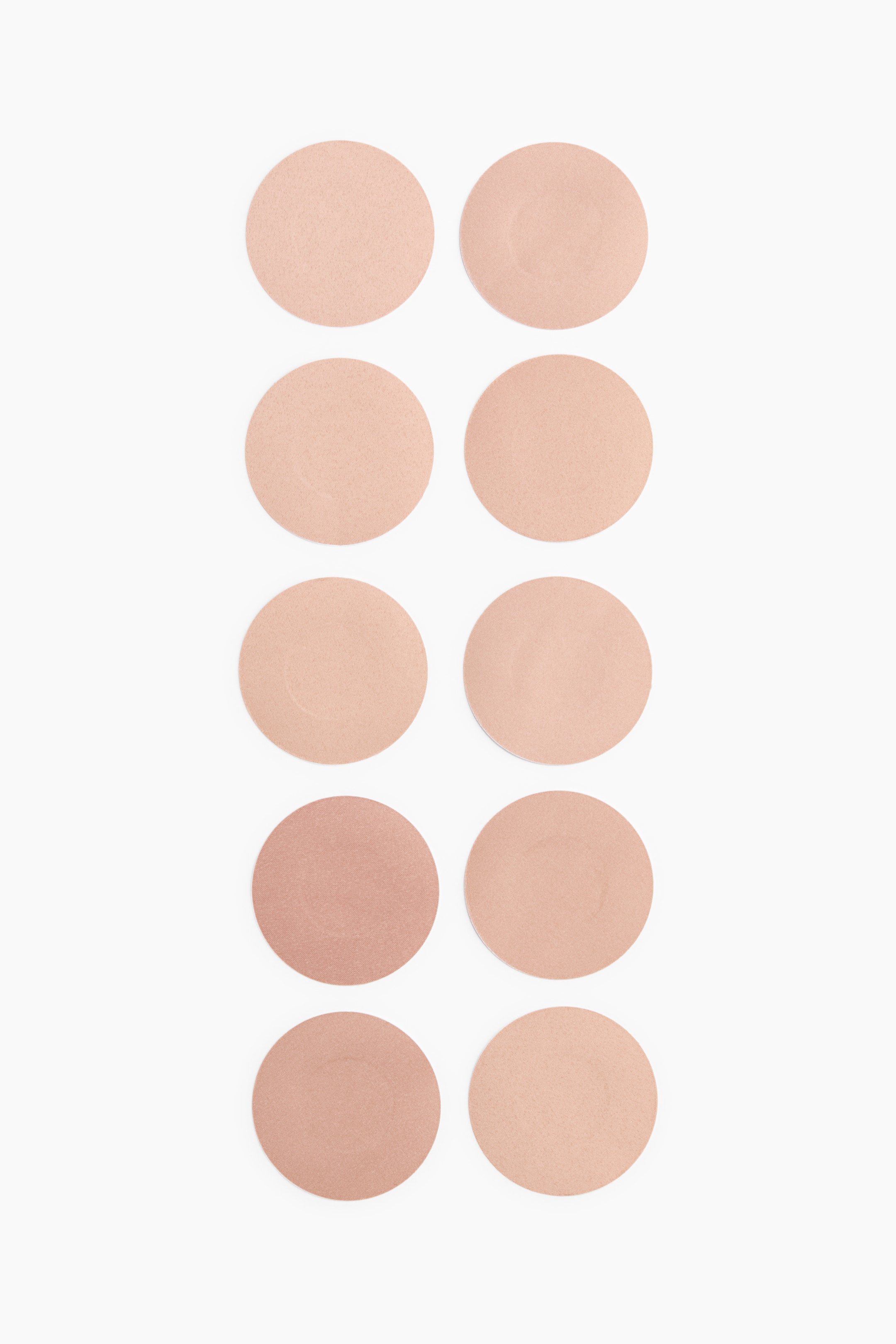 View larger image: Soft, self-adhesive nipple covers are presented as a set of ten pieces. They are arranged in two vertical columns, with each circular cover facing forward and featuring a smooth, matte surface in a range of nude tones from light beige to medium brown.