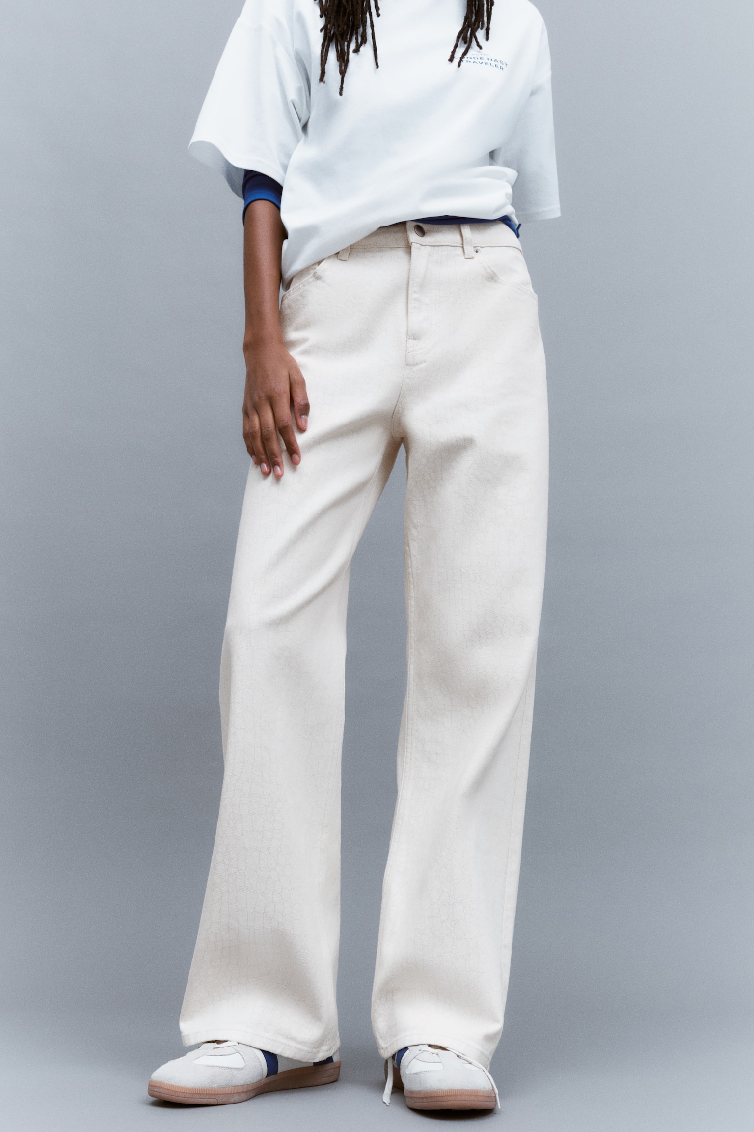 Off-white, high-waisted denim jeans with a straight-leg cut and five-pocket styling are worn by the model. The jeans are styled with a partially tucked white t-shirt and white sneakers. - 1