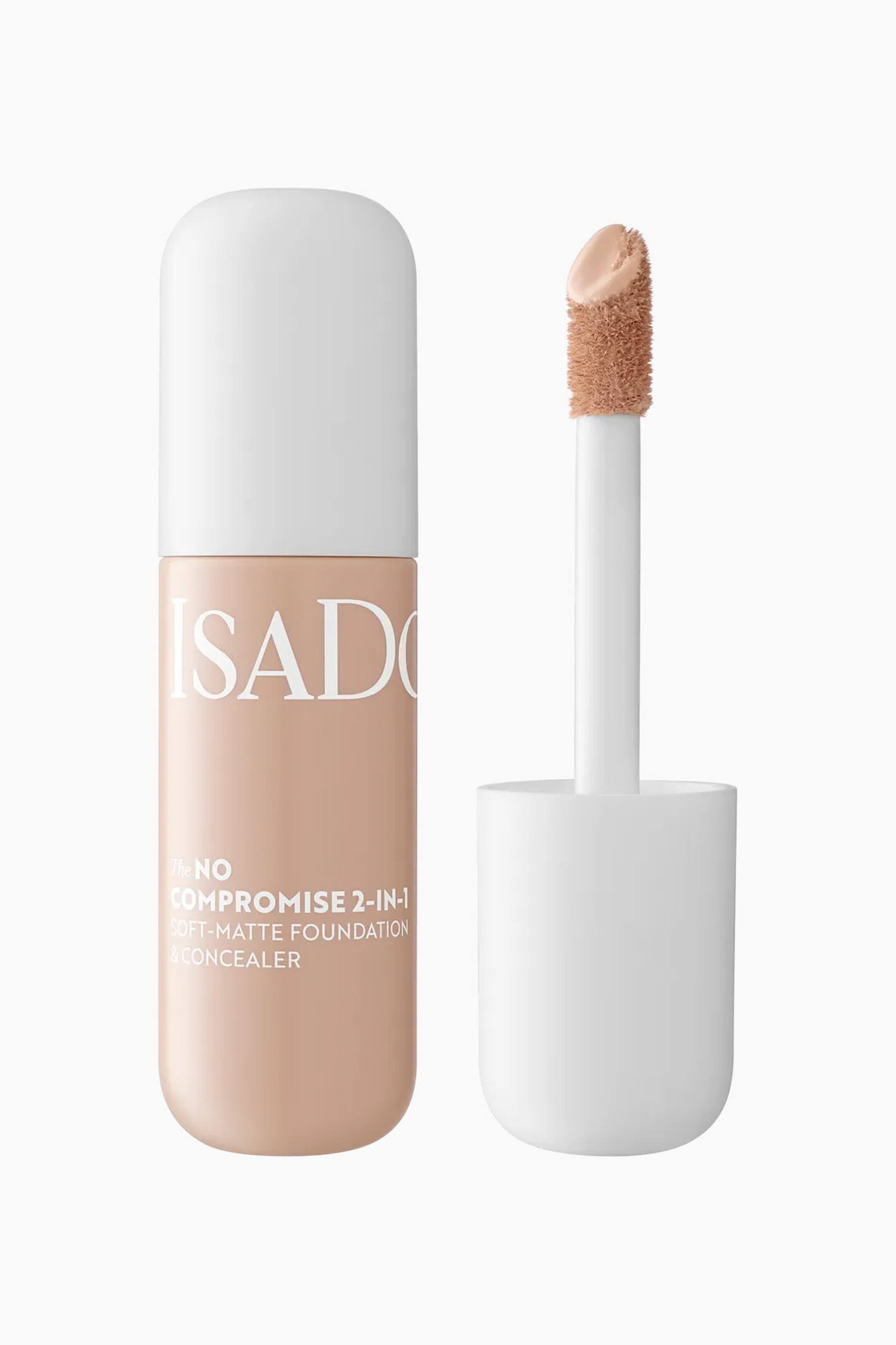 Visa större bild: En 2-i-1 foundation- och concealerprodukt står upprätt och visar en rundad cylindrisk flaska tillsammans med sin avskruvade applikatorstav. Flaskan visar en ljus medium beige flytande formula med vit text, medan staven har en stor, vinklad doe-foot-applikator täckt av den matchande makeupen.