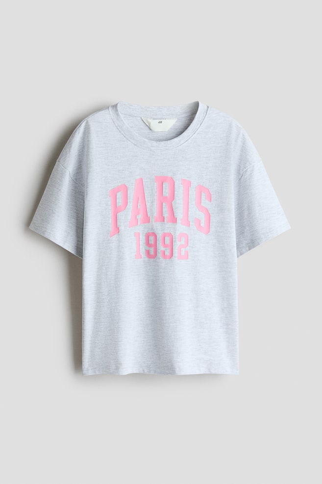 A light grey marl cotton jersey T-shirt is displaying its front, featuring a pink 'PARIS 1992' graphic print. It is designed with a round, rib-trimmed neckline and dropped shoulders. - 1
