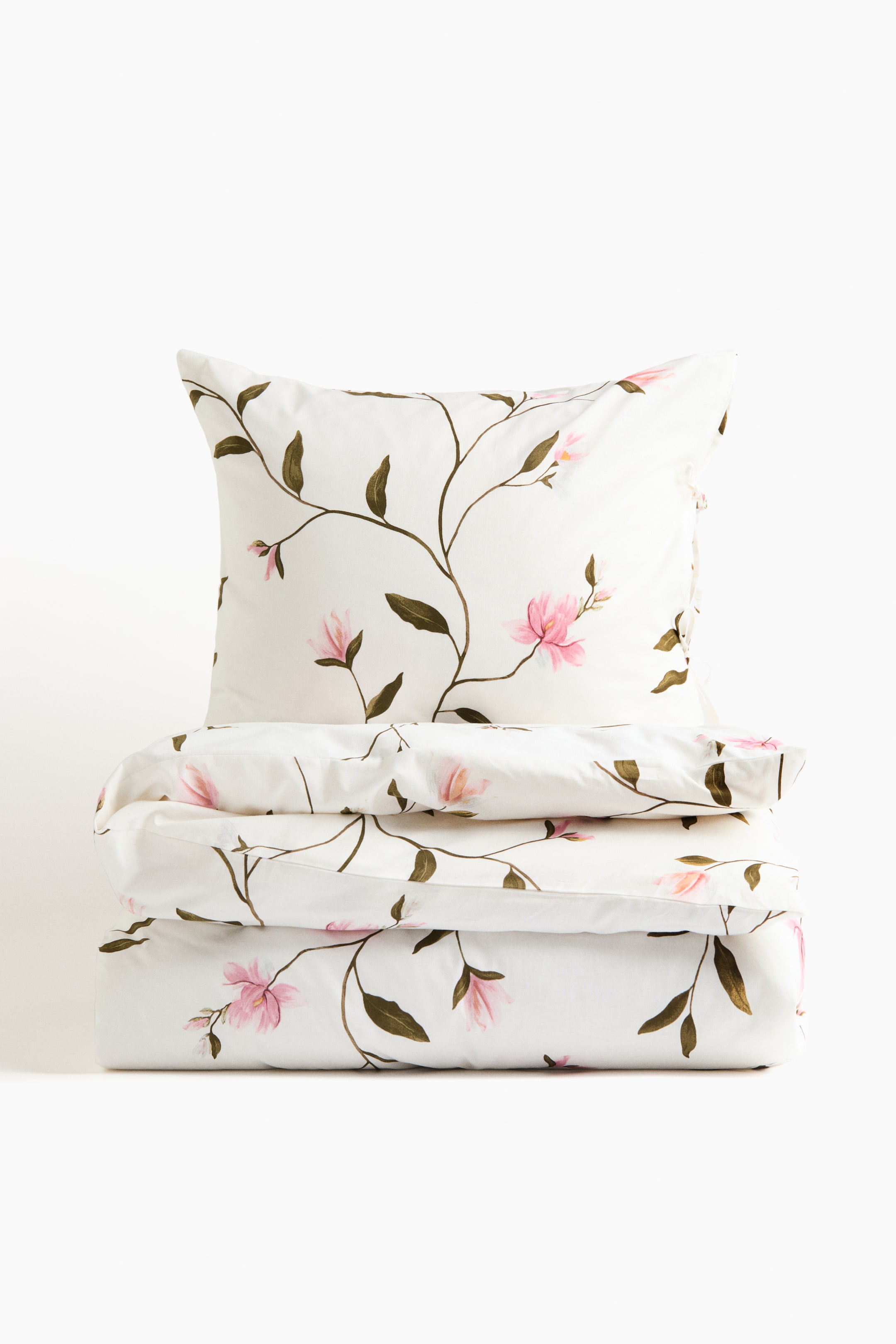 View larger image: A bedding set is featuring a white base with a repeating pattern of winding brown-green vines and delicate pink blossoms. A pillowcase is standing upright, facing FRONT, above two neatly folded rectangular pieces of matching fabric.