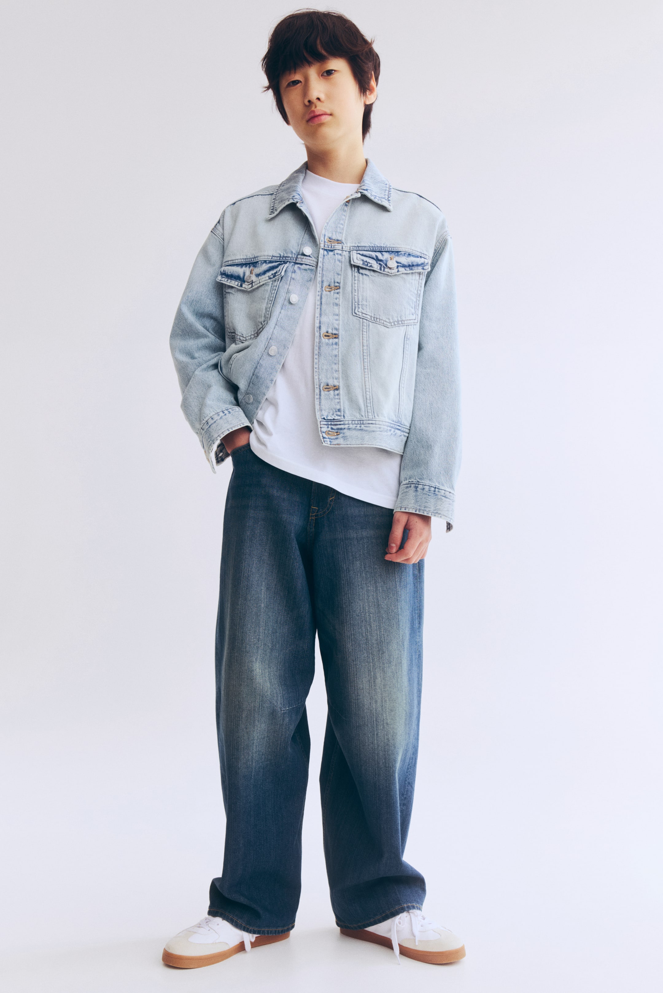 Agrandir l'image: Le devant du jean 5 poches en denim délavé présente une coupe ample au niveau des hanches et des cuisses avec une fourche basse, une braguette zippée avec fermeture par bouton, des jambes barrel aux ourlets effilés et des coutures latérales torsadées.