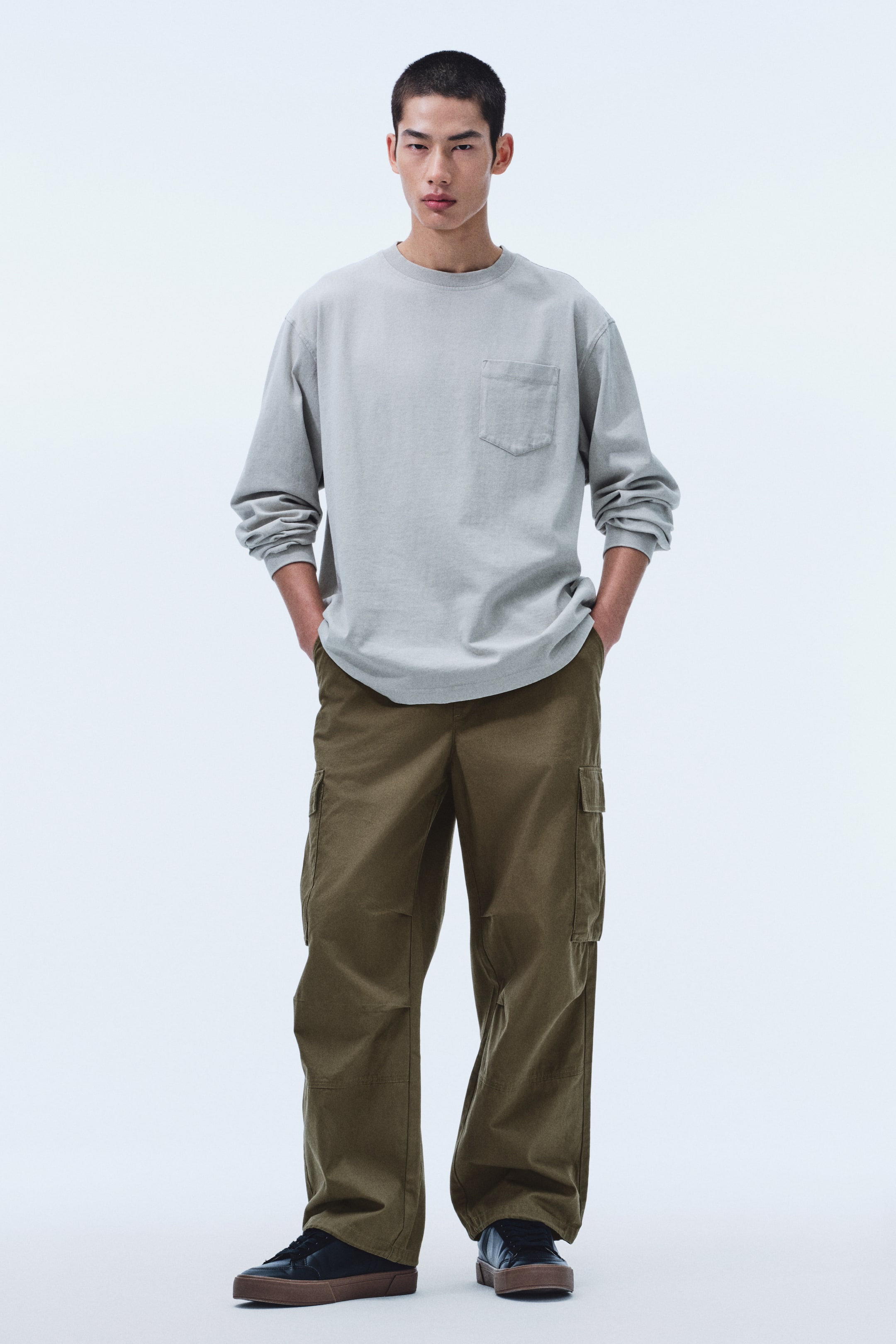 View larger image: Olive-green cargo pants feature a loose, wide-leg fit with rectangular flap cargo pockets on the side of each thigh. The pants present a relaxed silhouette, pooling slightly at the ankles.