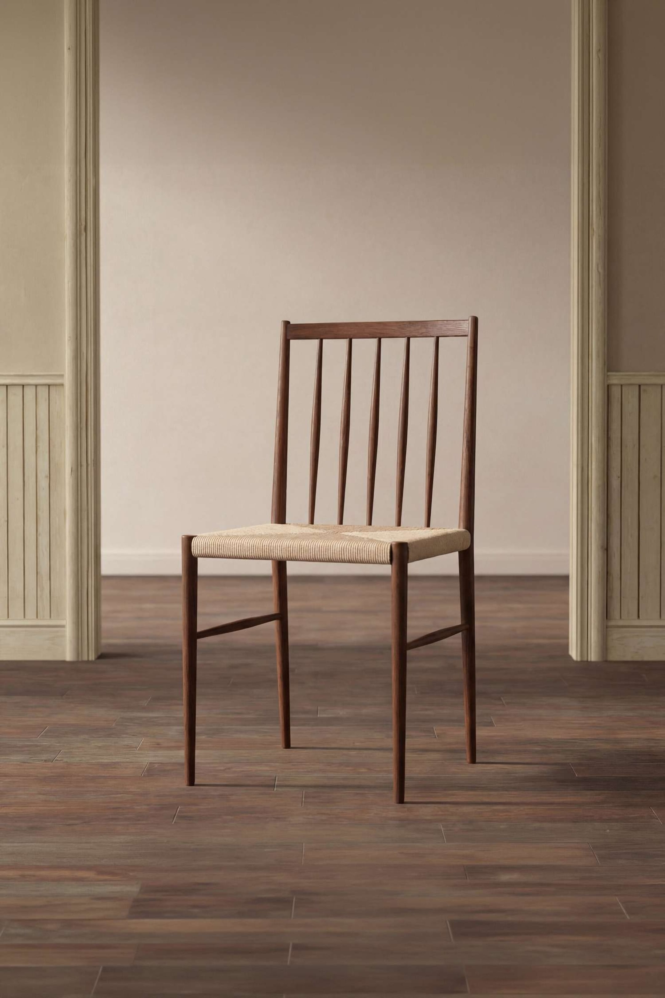 Agrandir l'image: Une chaise en bois brun foncé est légèrement inclinée vers la droite, montrant un dossier à barreaux avec des fuseaux verticaux effilés et une assise tressée de couleur claire.