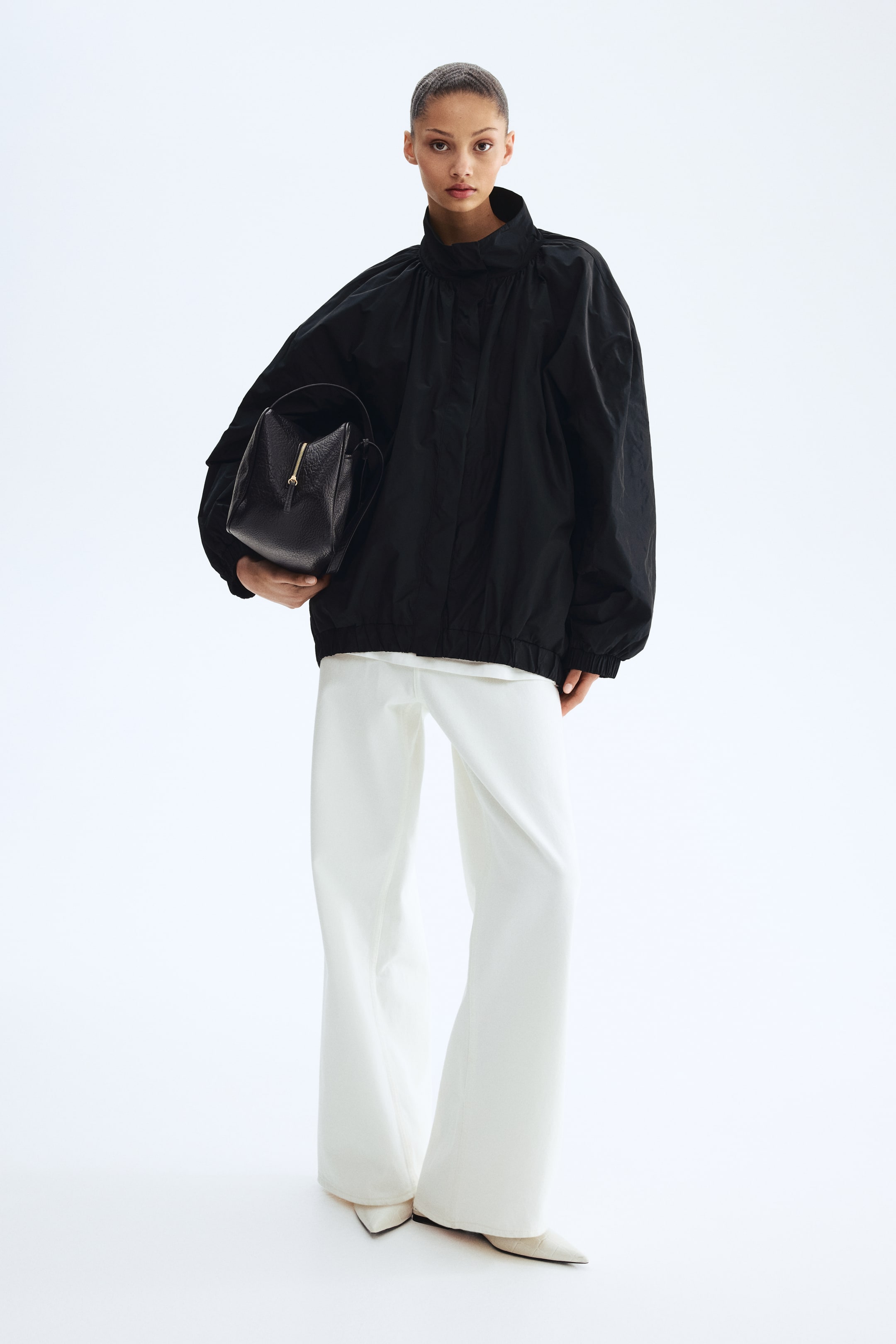 Ingrandisci l'immagine: La borsa in pelle nera martellata è tenuta in mano, caratterizzata da una forma strutturata con una chiusura a zip dorata nella parte superiore e una sottile tracolla visibile sul lato.