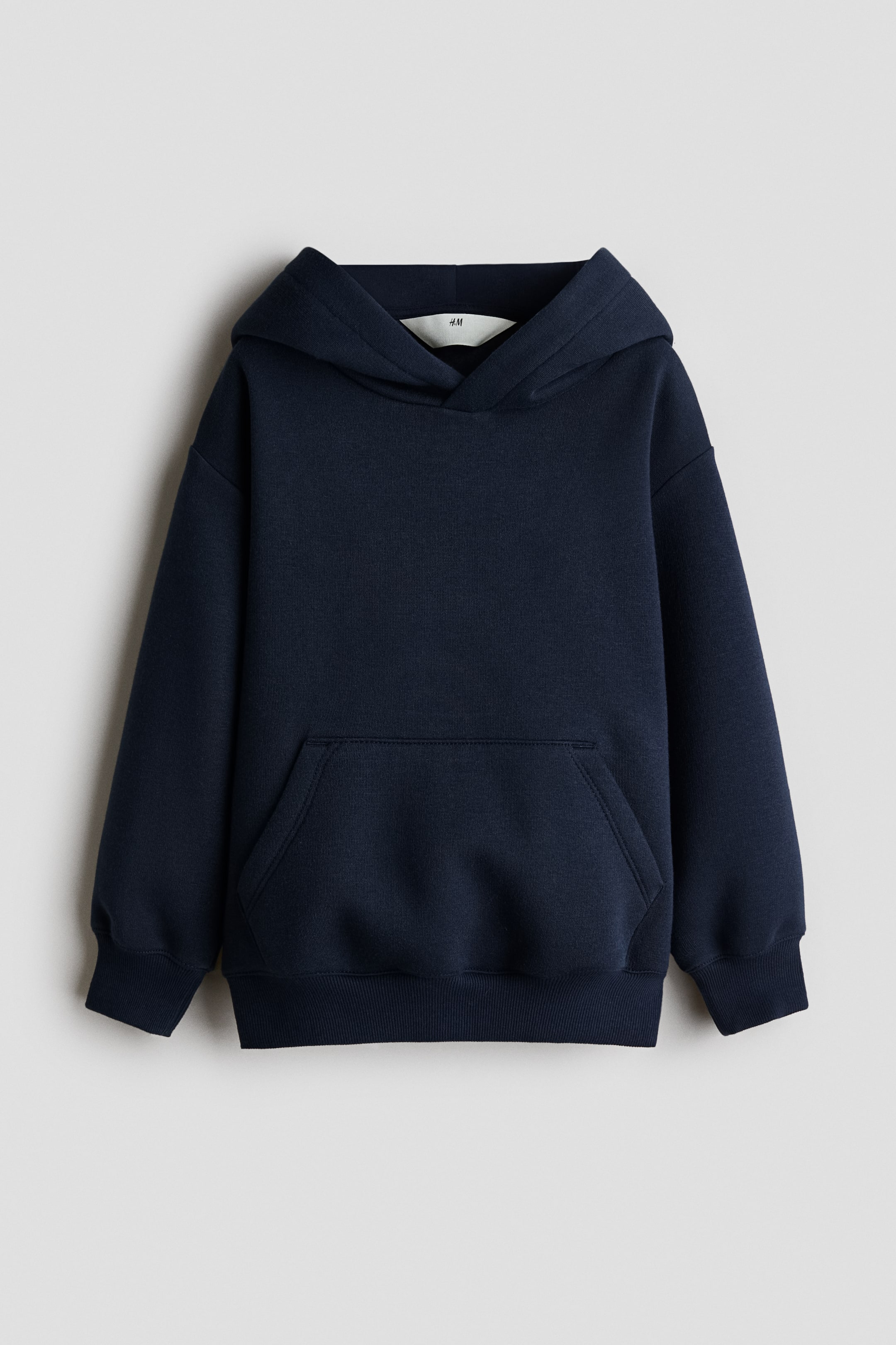 Xem ảnh lớn hơn: Một chiếc áo hoodie màu xanh navy đậm được chụp chính diện, nổi bật với mũ trùm chéo và phần vai xuôi nhẹ. Áo sweatshirt tay dài có túi kangaroo phía trước cùng bo gấu và cổ tay rộng, dệt gân.