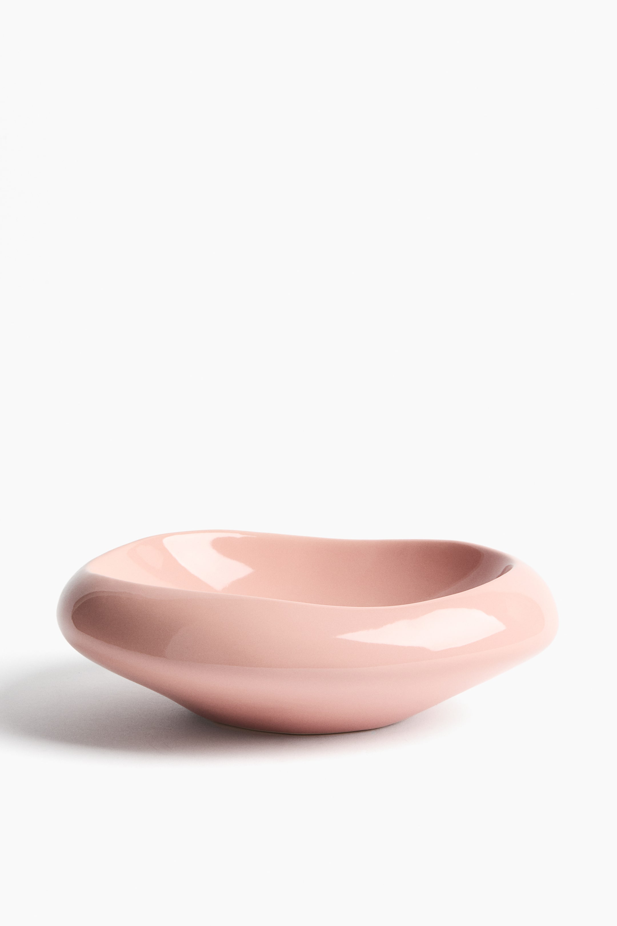 View larger image: A light pink, glossy ceramic bowl is showcasing an elongated, organically curved form with a shallow interior and smoothly rounded rim.