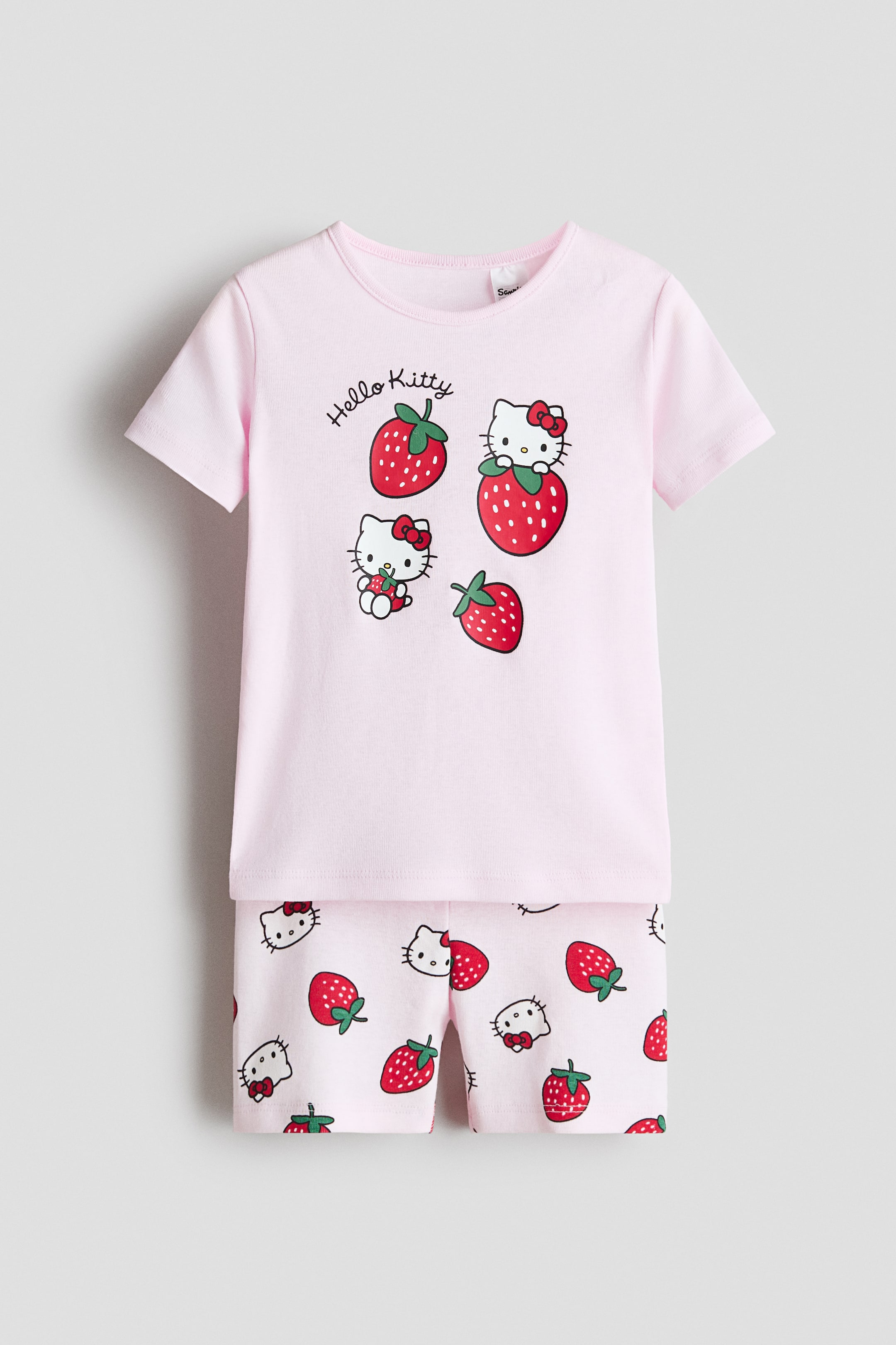 View larger image: Pyjamas in light pink printed cotton jersey are displayed from the front, featuring a short-sleeved top with a round, rib-trimmed neckline and a central print of "Hello Kitty" text, Hello Kitty characters, and strawberries, along with matching shorts. The shorts showcase an all-over repeating pattern of Hello Kitty faces and strawberries.