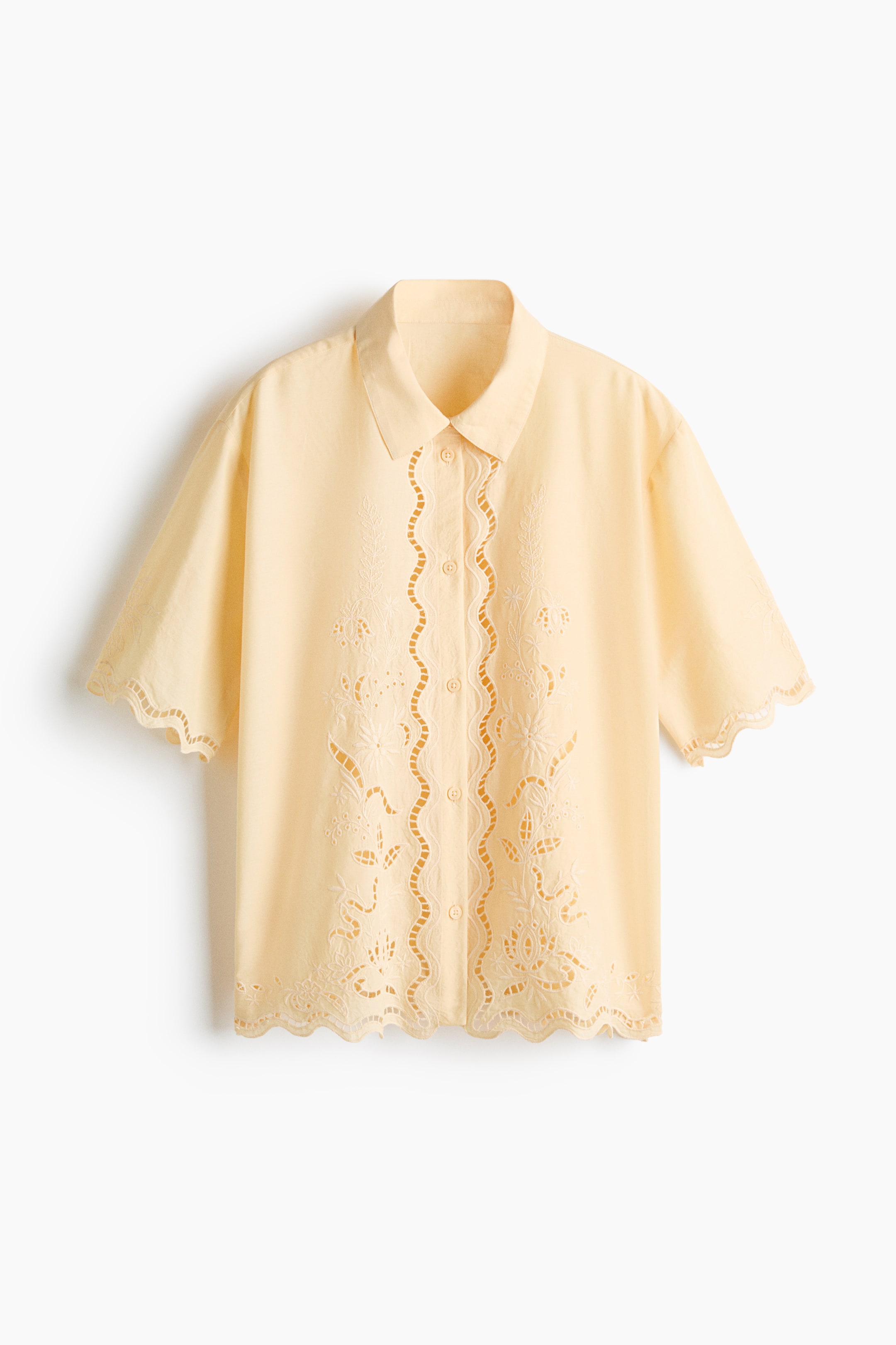 View larger image: A light yellow short-sleeved shirt, viewed from the front, crafted from a cotton weave. It showcases a collar, buttons down the front, and broderie anglaise detailing with scalloped edges on the sleeves and hem.