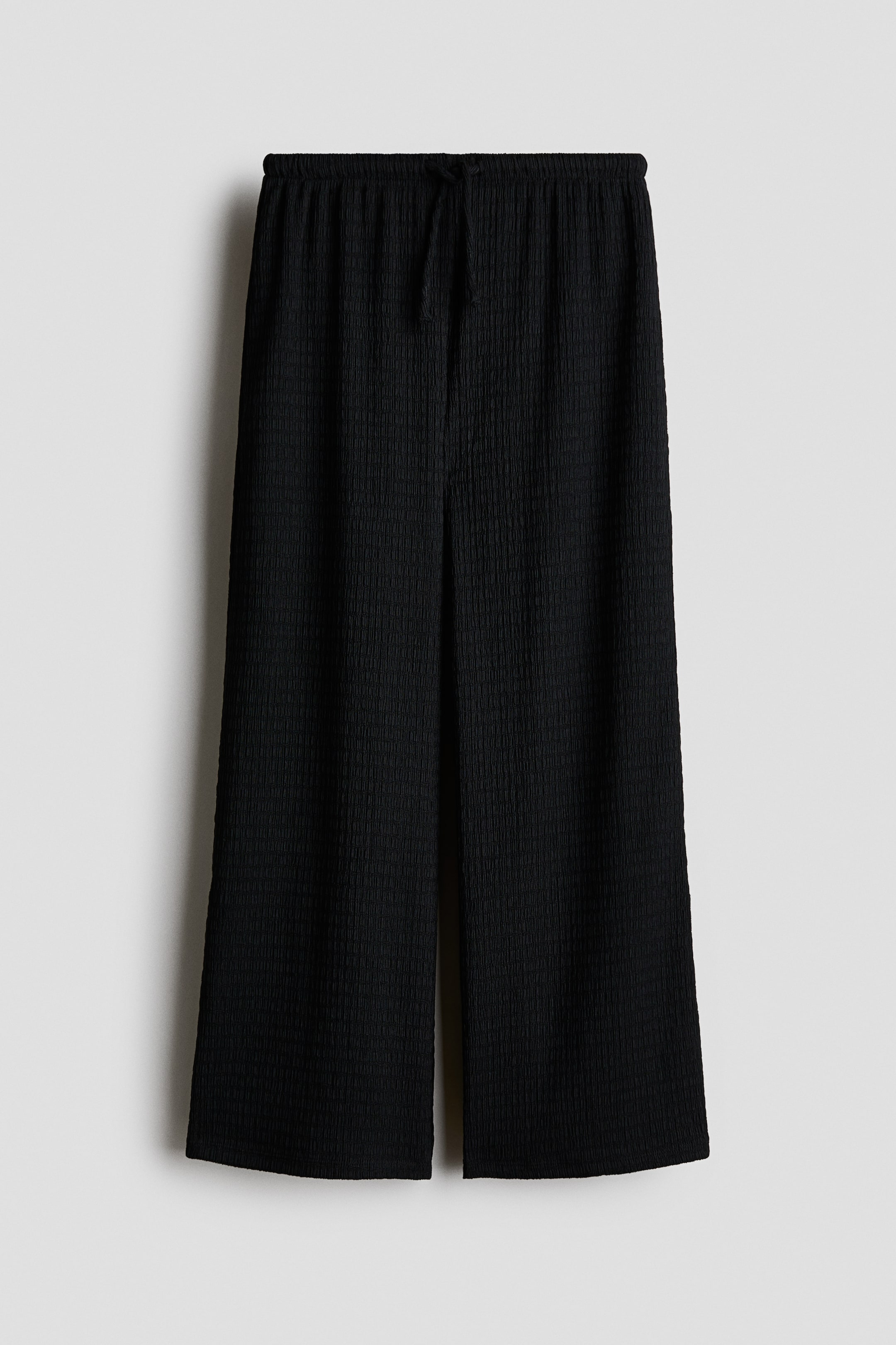 View larger image: The black trousers showcase a textured jersey fabric on the front. They come with an elasticated drawstring waist and straight legs.