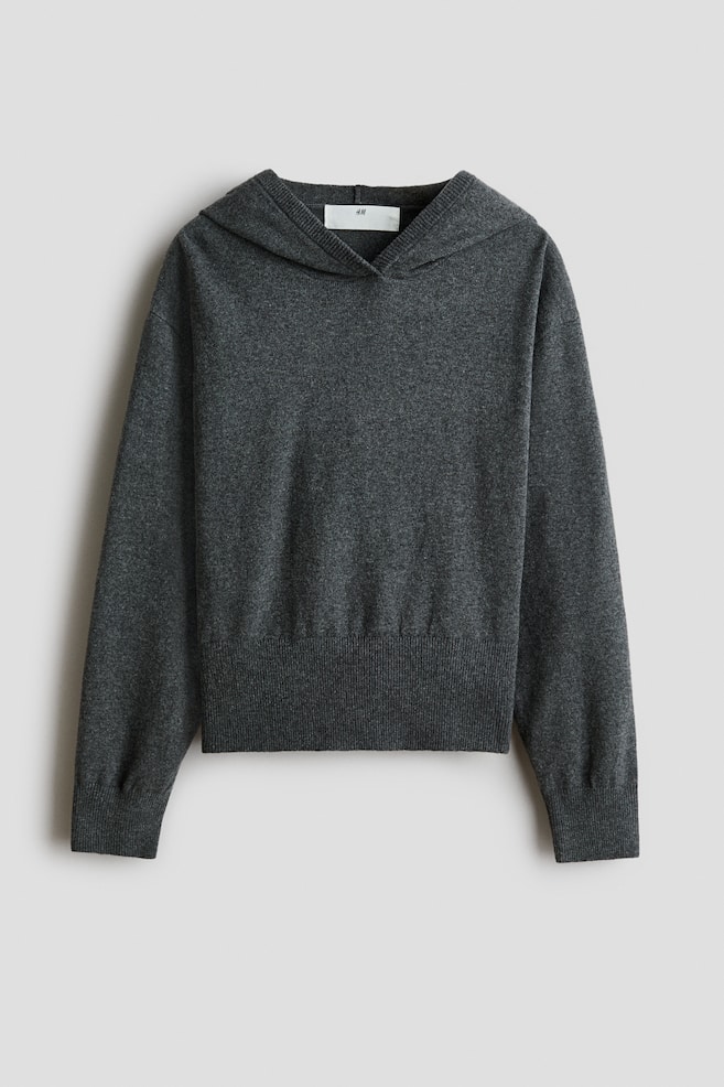 Una felpa con cappuccio in maglia fine di colore grigio scuro Ã¨ mostrata frontalmente, con una silhouette rilassata e cappuccio incrociato. Il capo Ã¨ progettato con spalle scese, maniche lunghe con ampi polsini a costine e un ampio orlo a costine coordinato. - 1