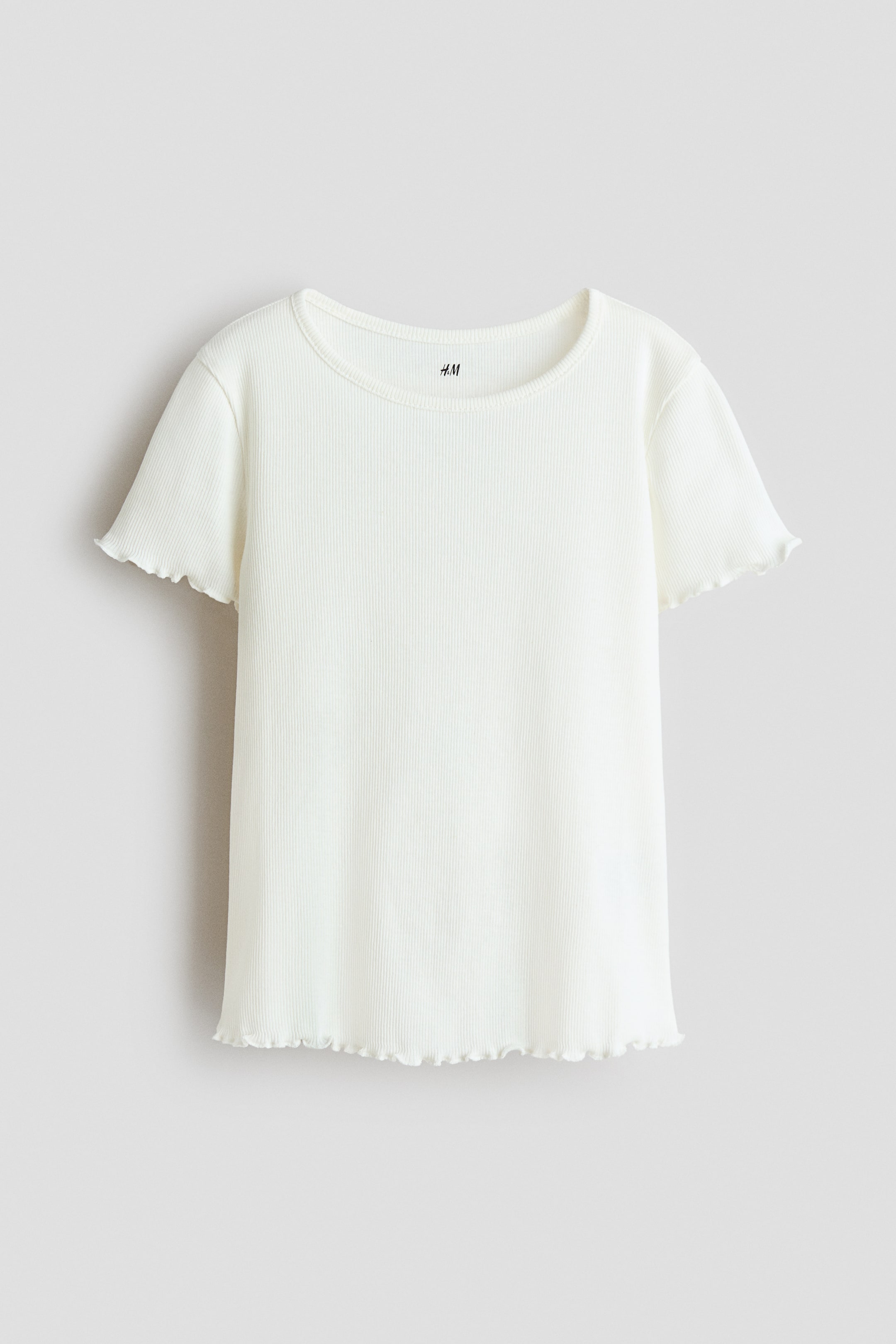 Ingrandisci l'immagine: Una t-shirt a coste in maglia color bianco sporco è posizionata di fronte. Presenta un girocollo, maniche corte e dettagli a bordo ondulato sui polsini delle maniche e sull'orlo inferiore.