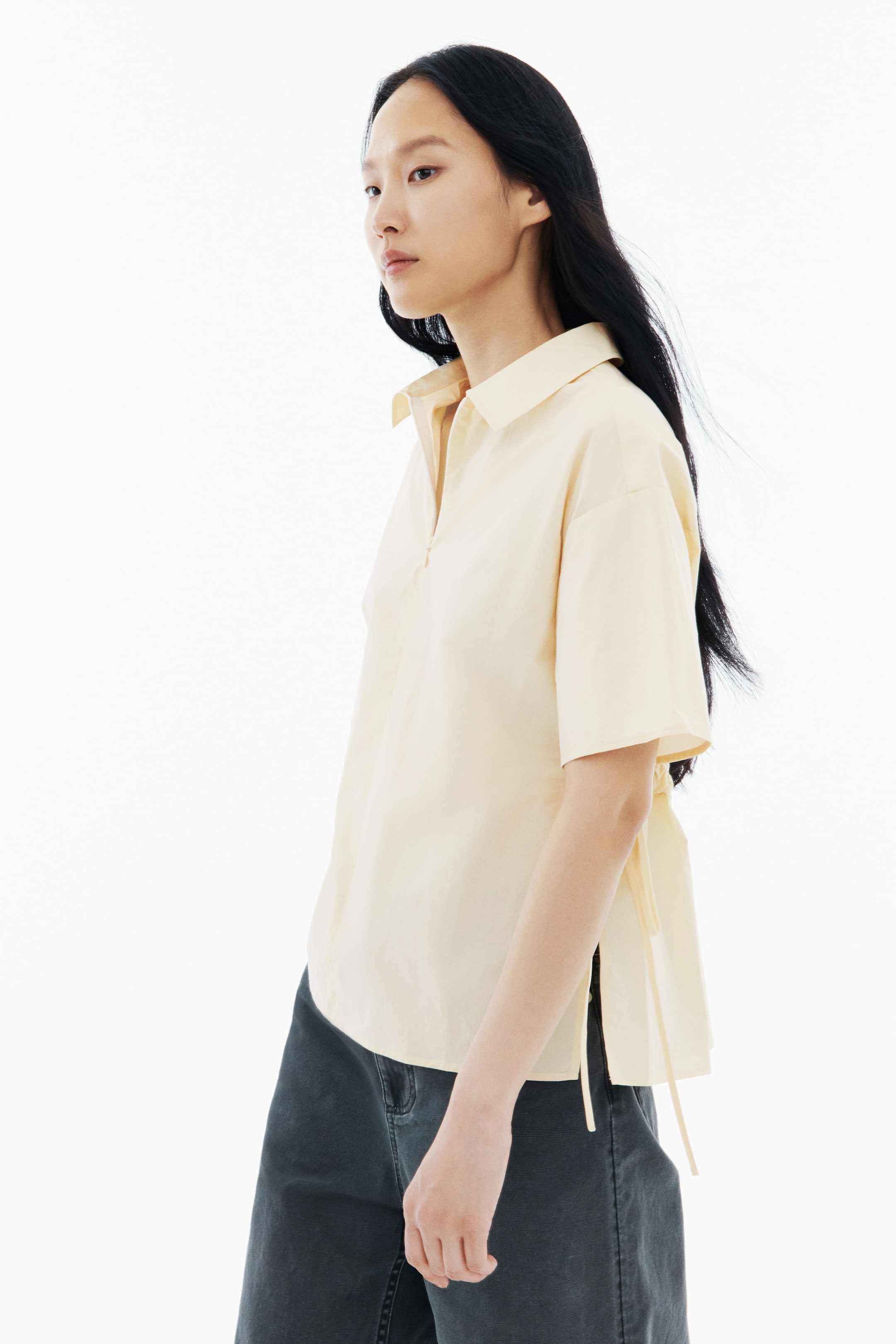 View larger image: The light yellow collared shirt features short sleeves and a V-neck placket. It showcases side slits with ties and offers a relaxed fit from a slight angle.